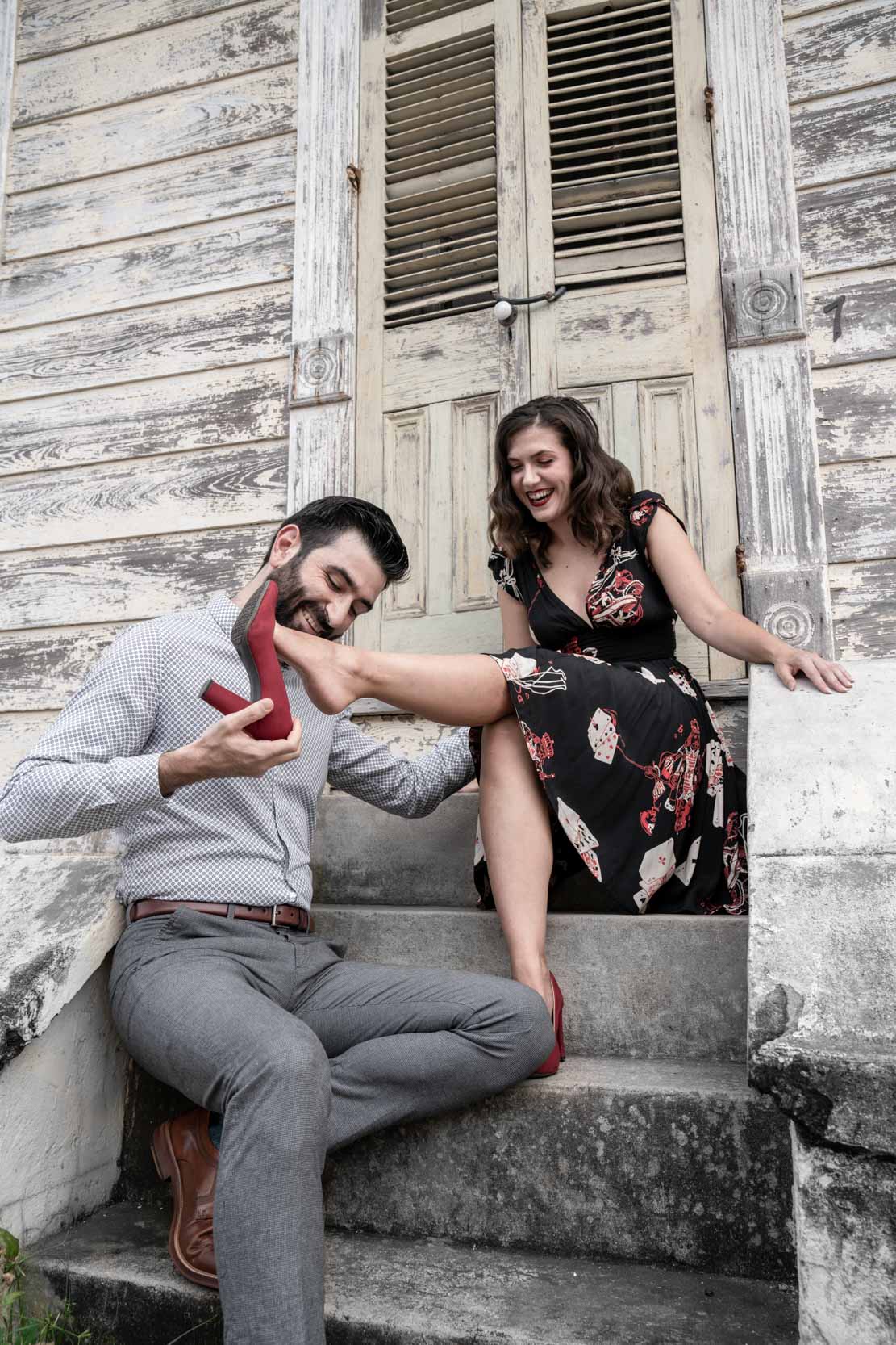 Man playing his girlfriend's red high heels in front of rustic house in the New Orleans French Quarter