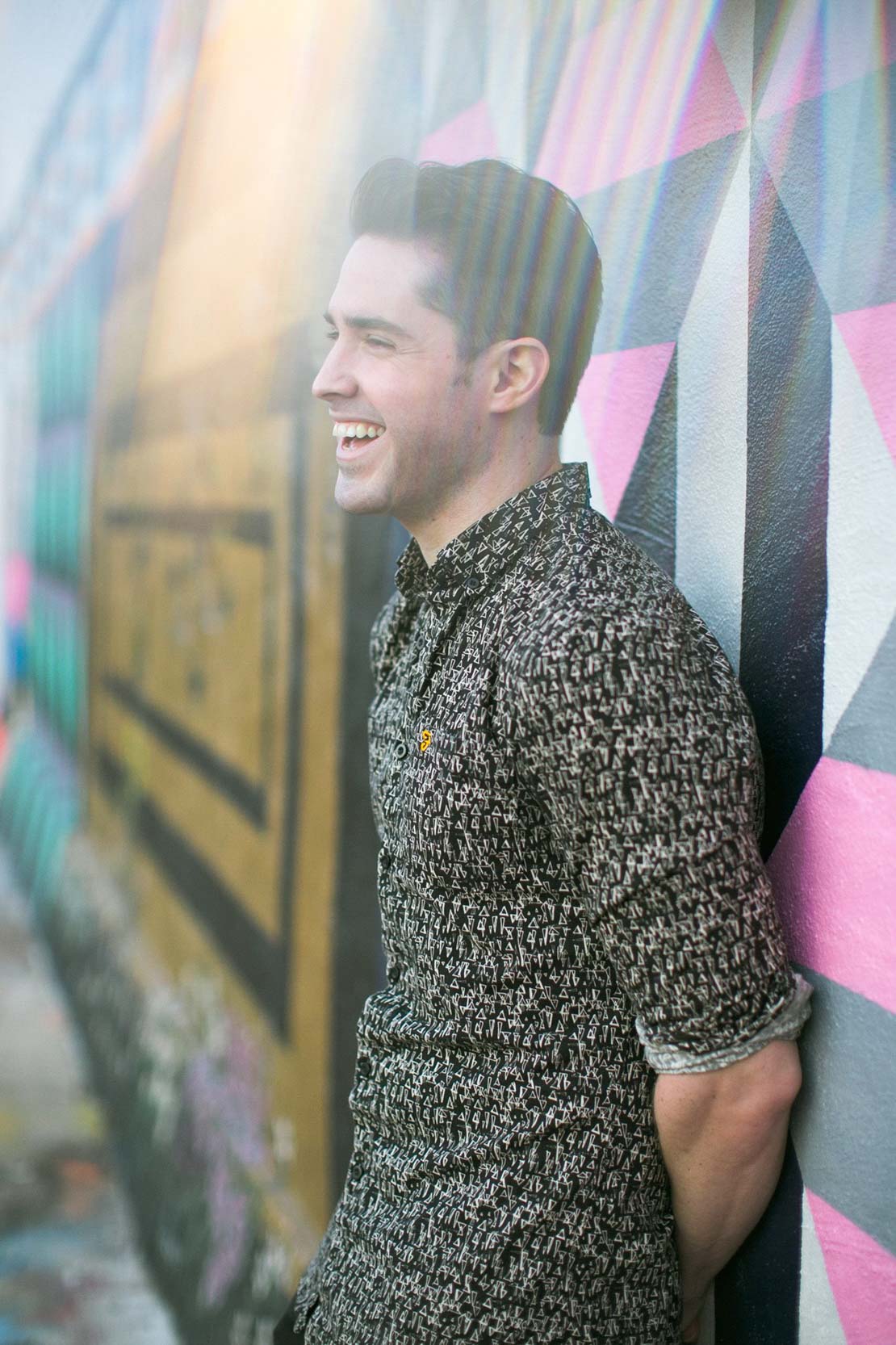 Ryan H Gray with Shades of Gray Photography laughing and smiling in front of a mural on Magazine Street in New Orleans