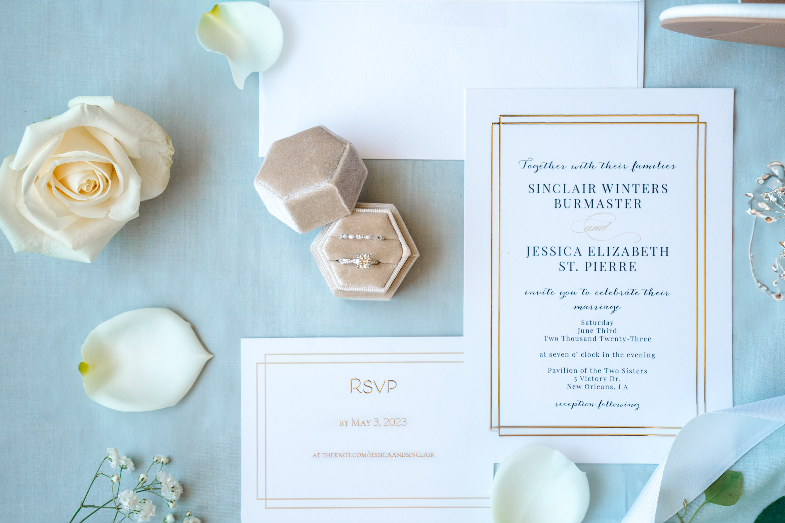 wedding flat lay of rings, invitations, rose petals