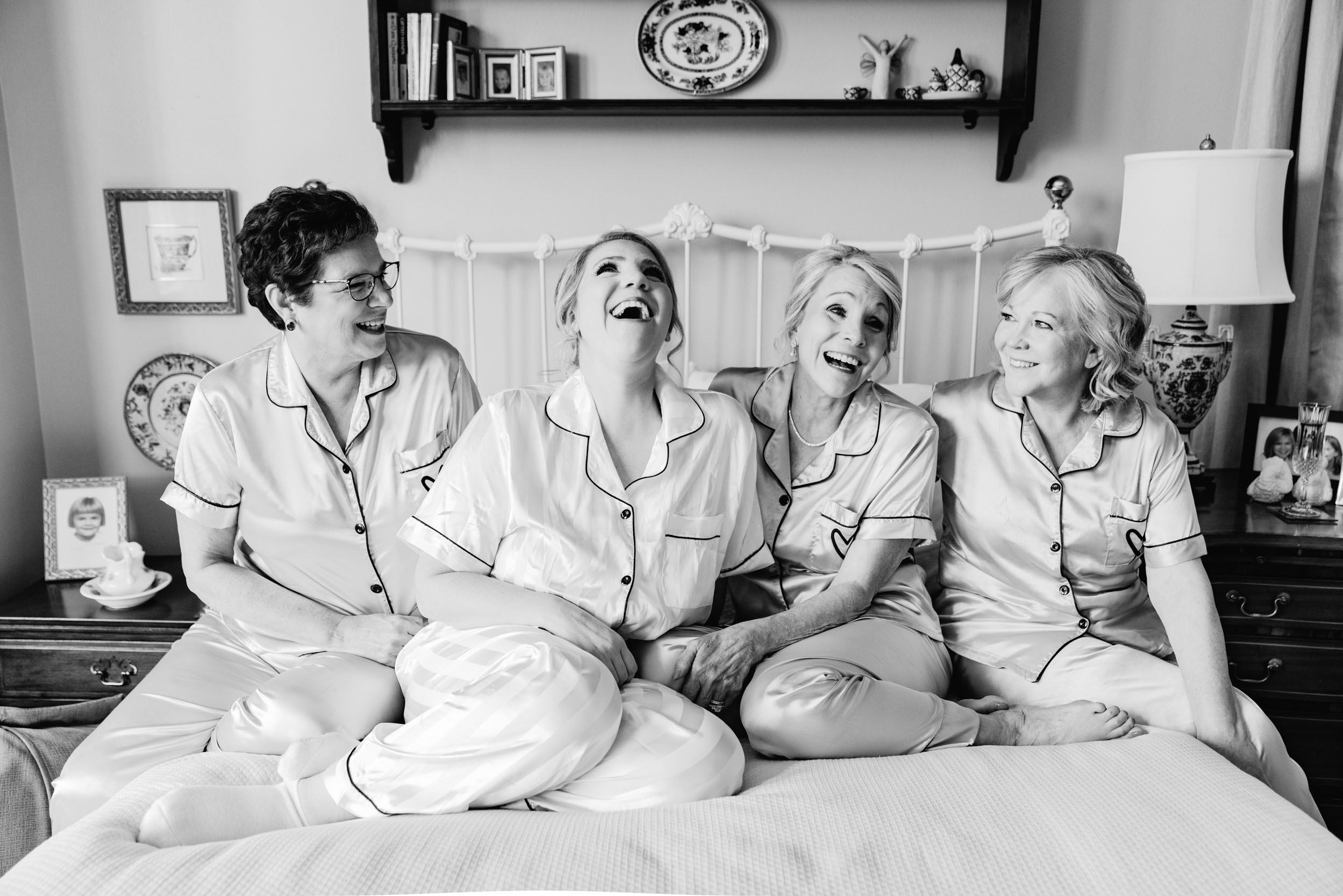 Bride and mother in robes laughing on bed in New Orleans