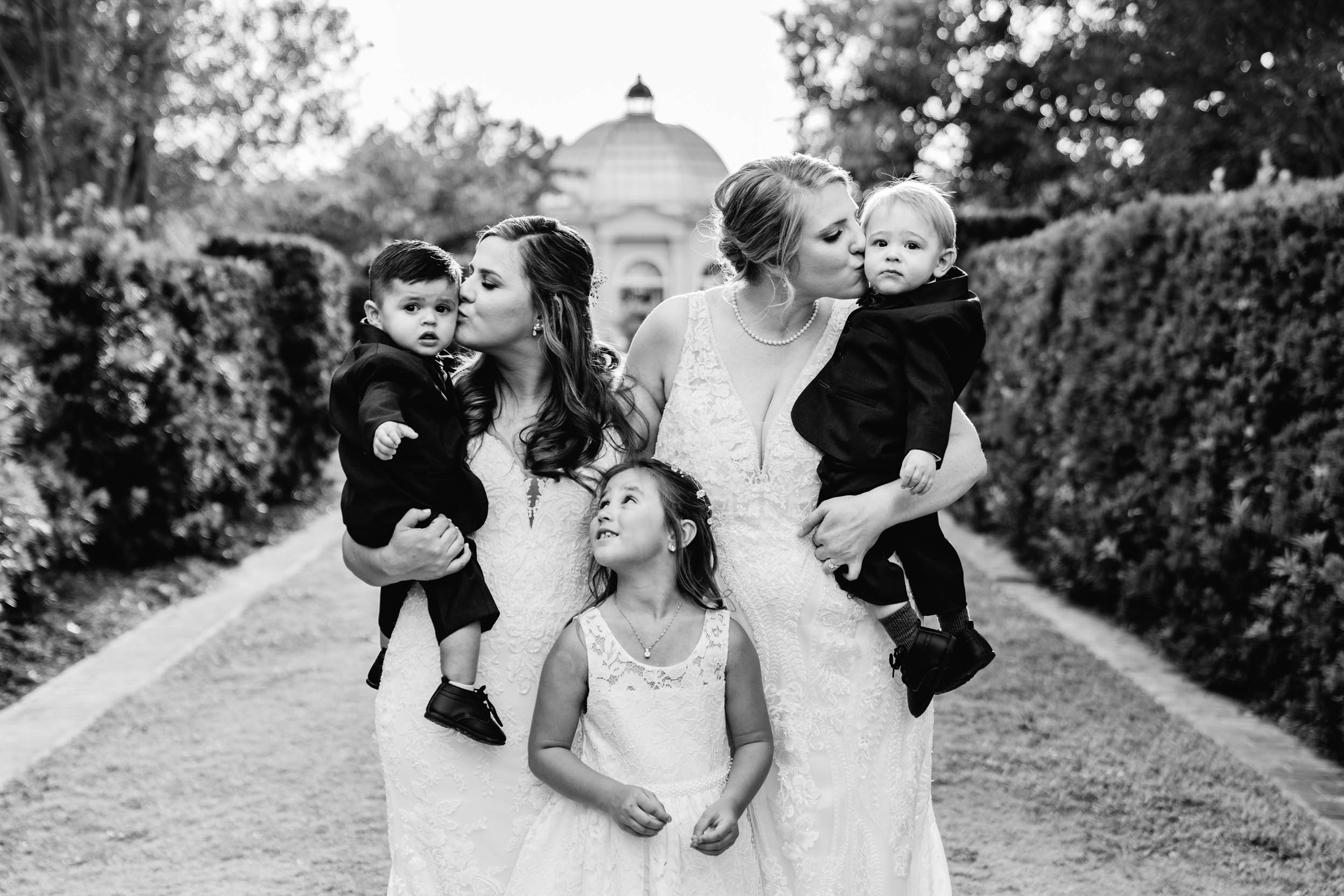 Brides kissing babies on wedding day at City Park Botanical Gardens