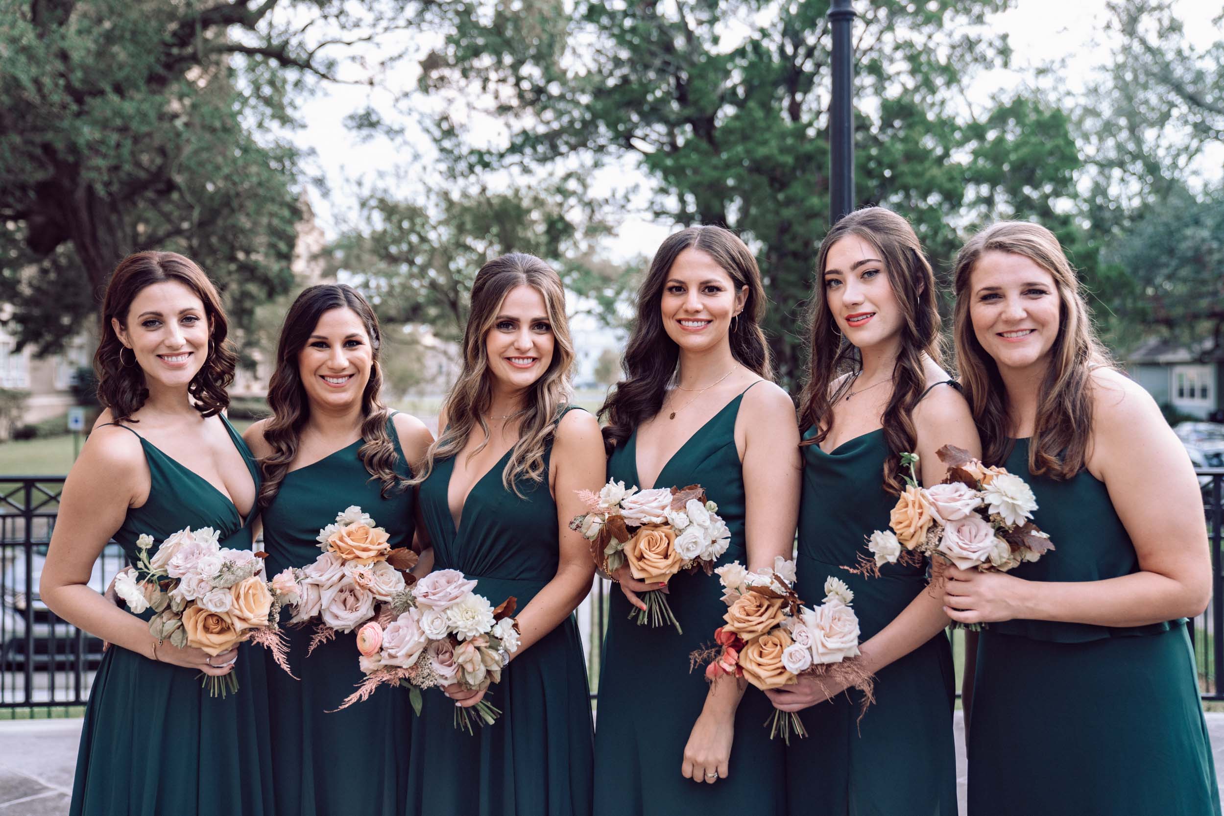 bridesmaids posing with green dresses and flowers and smiling in front of Ursuline Church in New Orleans