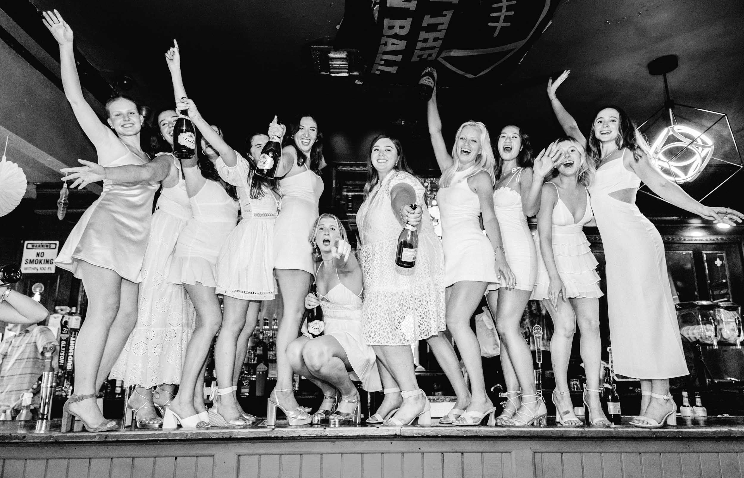 graduation students dancing on bar top with wine bottles