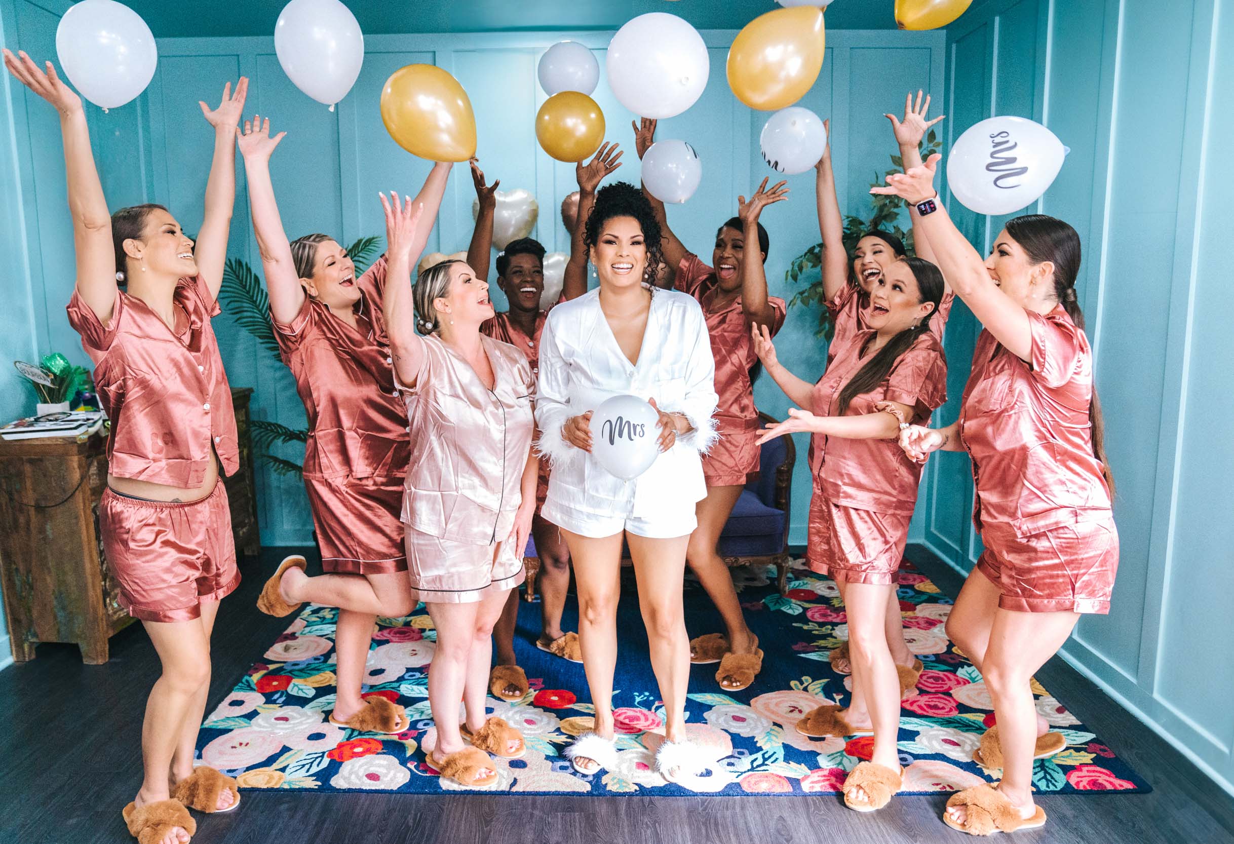 African American bride and her bridesmaids throwing balloons and celebrating in robes on wedding day