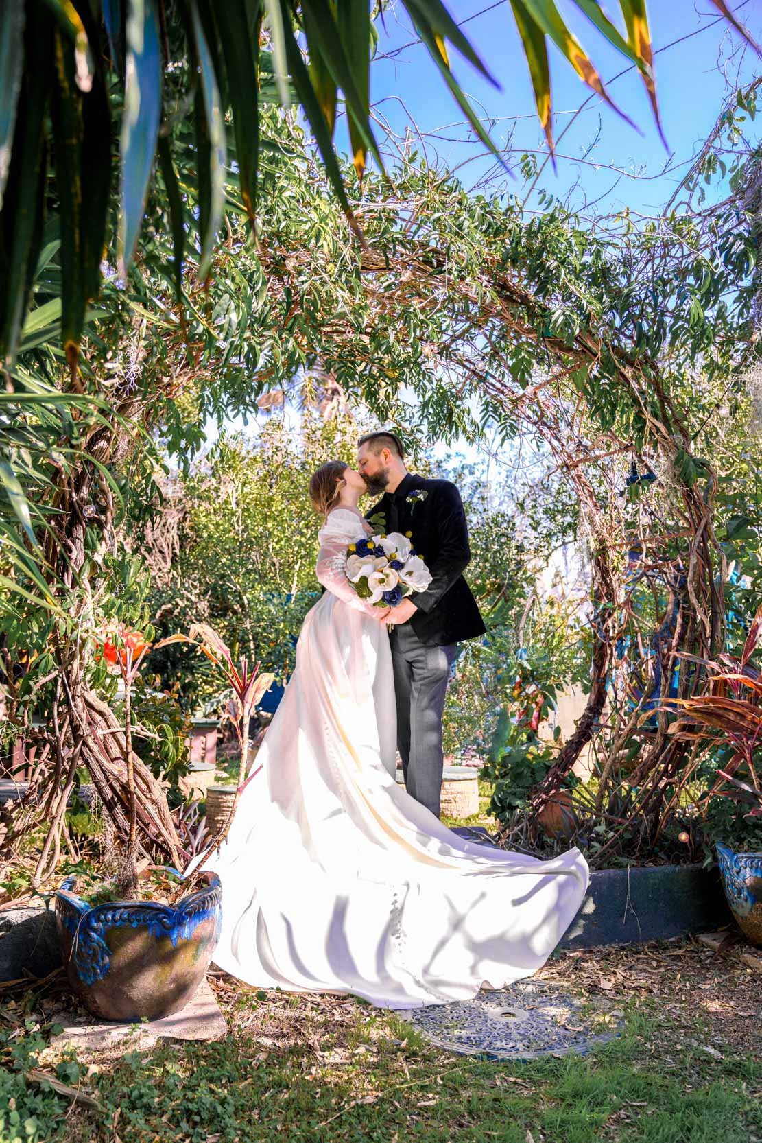 bride and groom kissing among tropical plants and arbor at Emerald Door in the New Orleans Bywater