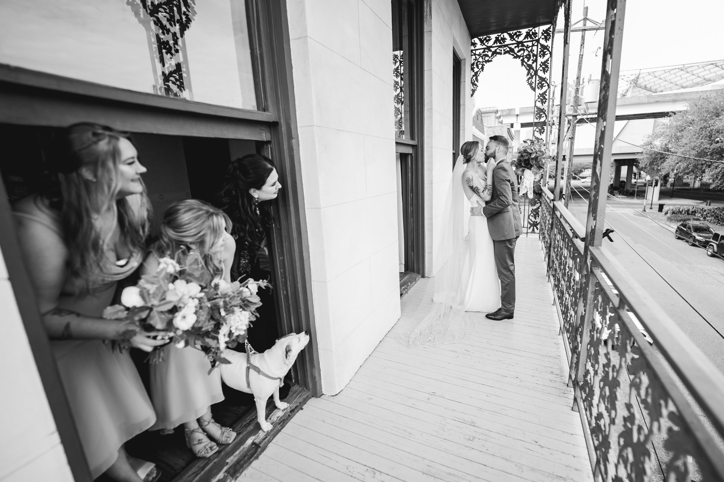 bride and groom kissing during their first look on balcony while bridesmaids watch at Margaret Place in New Orleans