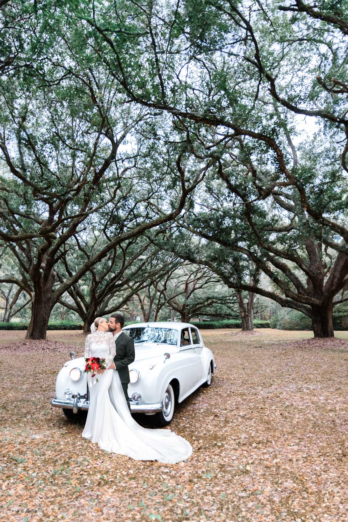 bride and groom kissing in front of Rolls-Royce and large oak trees at The Greenwood Covington, Louisiana