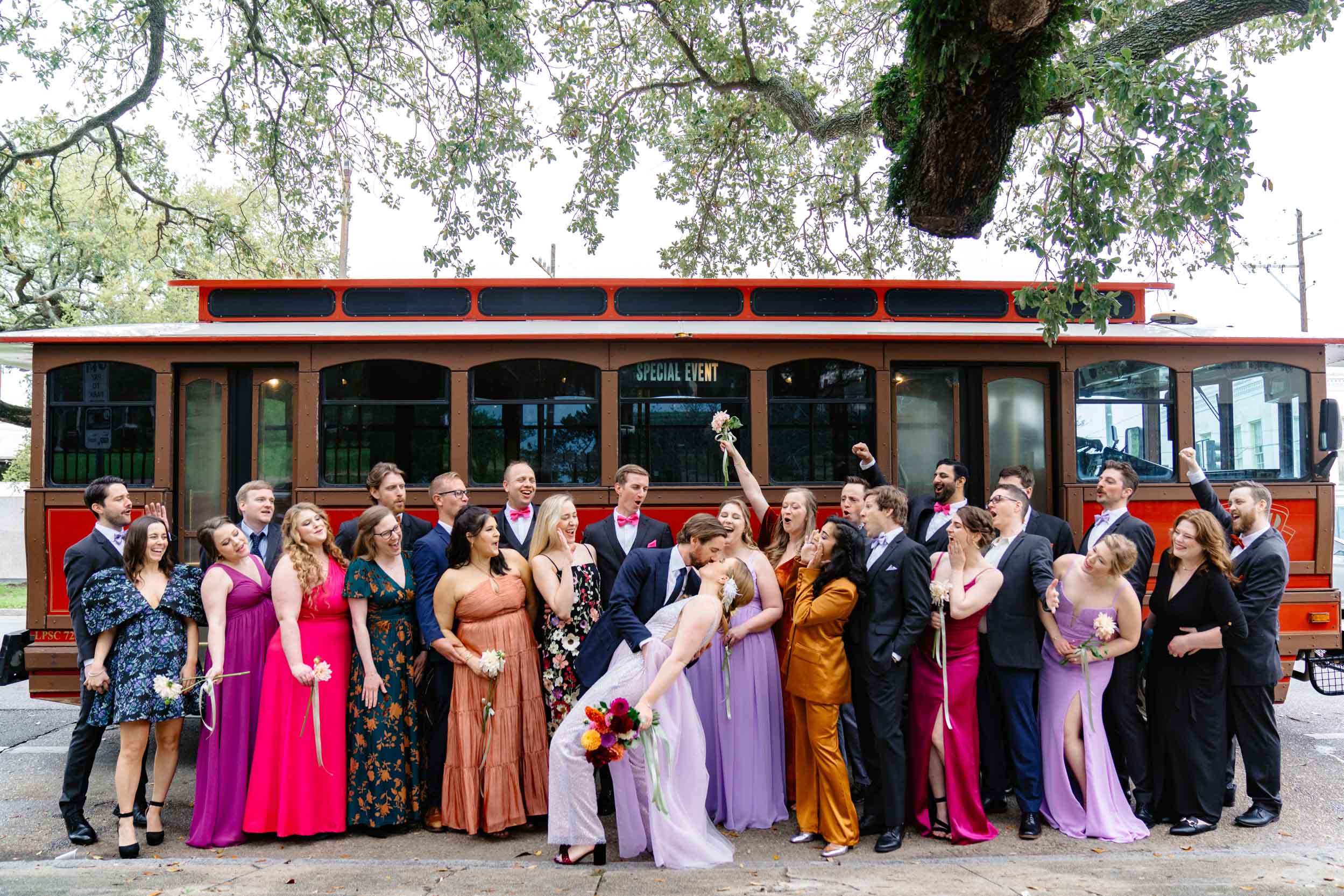 bride and groom kissing next to wedding party in front of trolley in the New Orleans Bywater at Washington Square Park