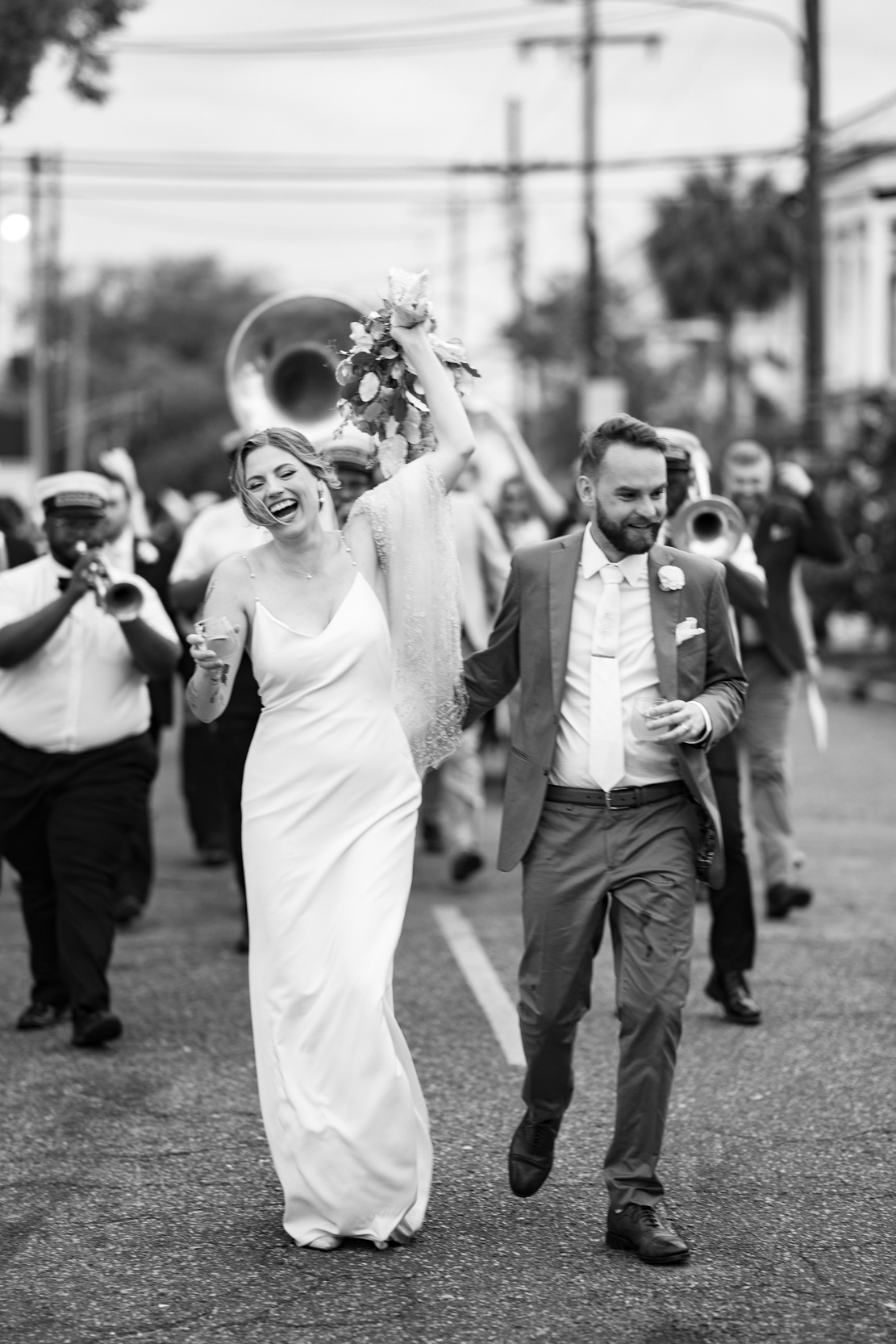 bride and groom laughing and walking during 2nd line band procession on wedding day in Lower Garden District in New Orleans