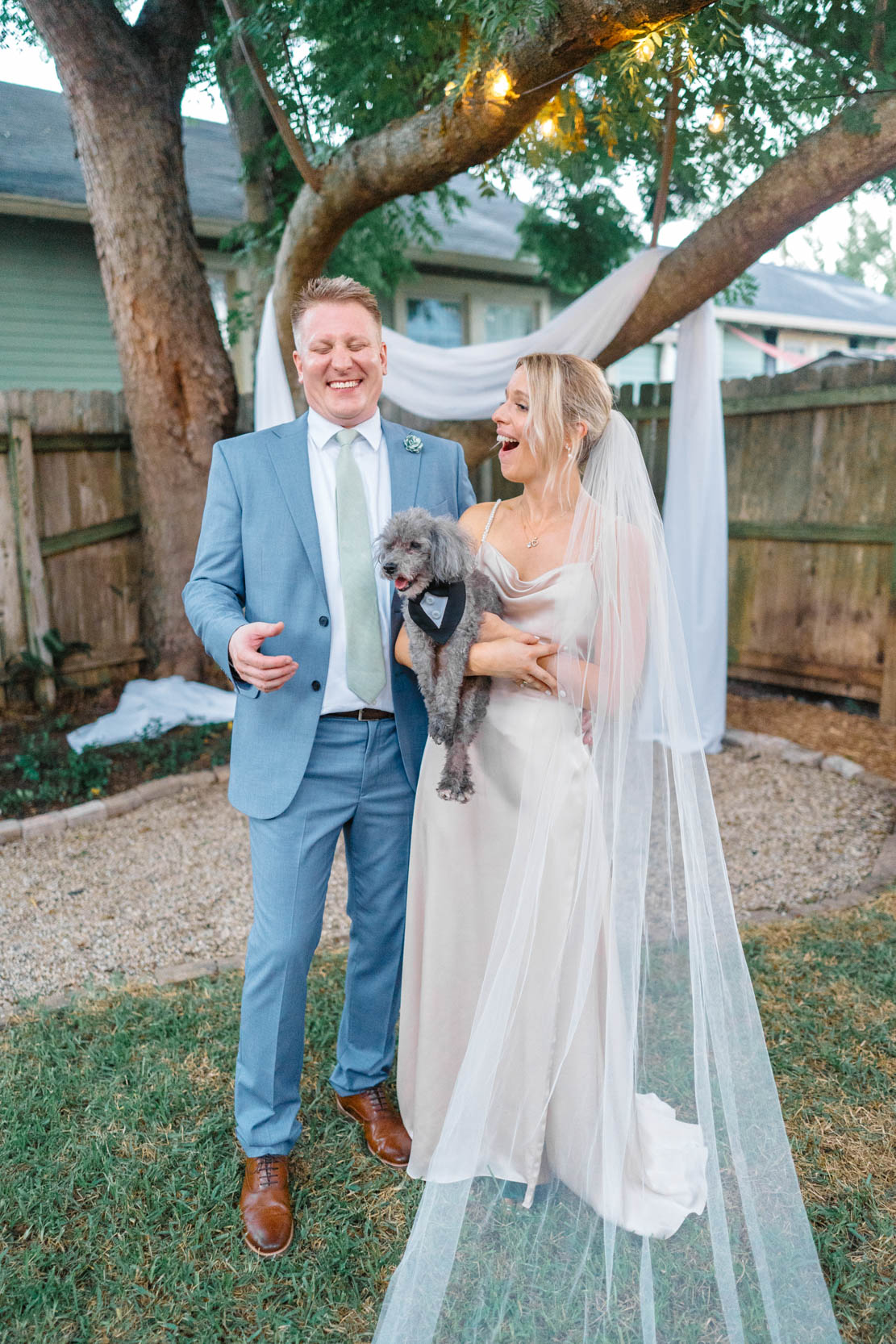 bride and groom laughing while holding their dog in backyard wedding in uptown New Orleans