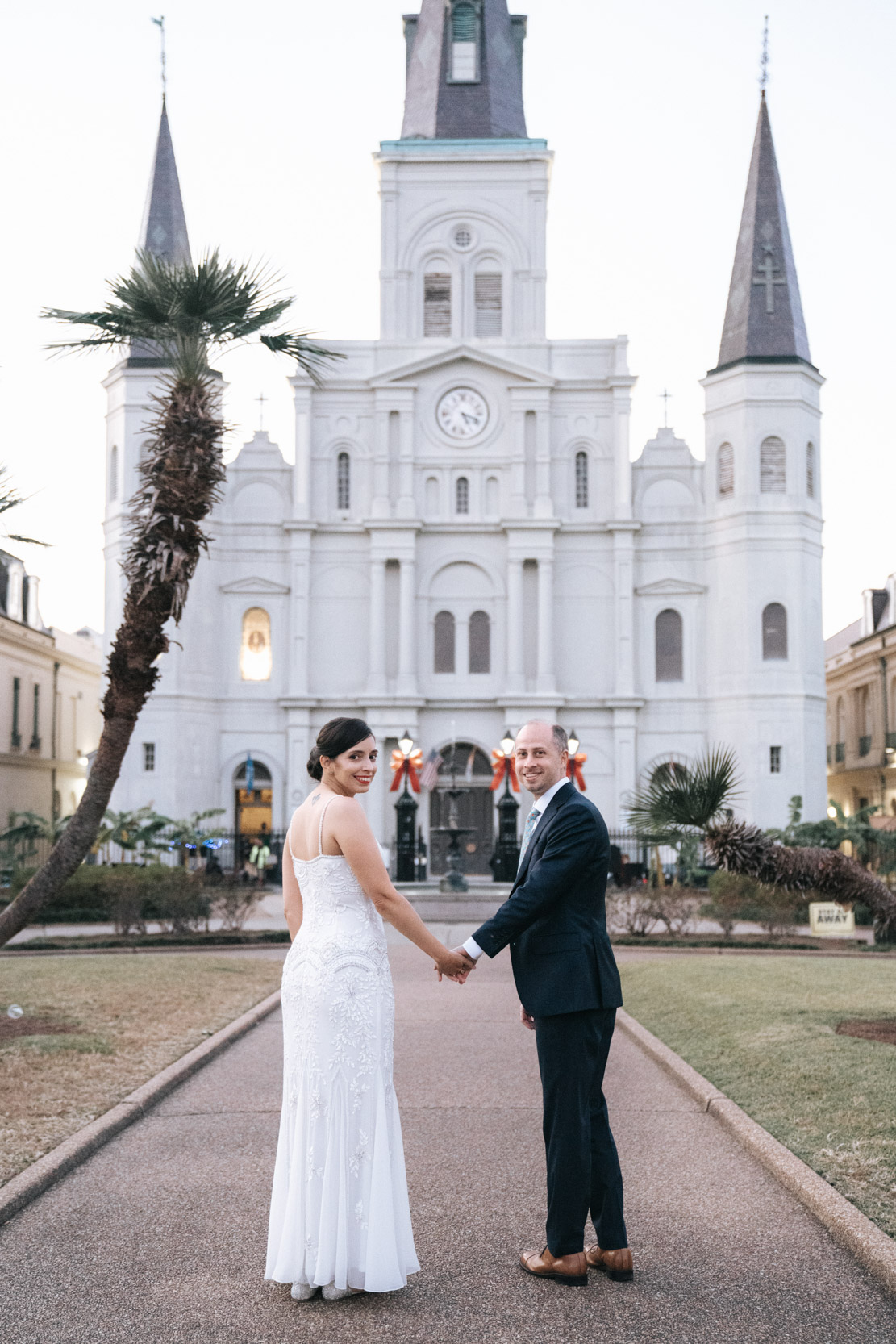 bride and groom looking back while walking in Jackson Square in New Orleans with St. Louis Cathedral in the background