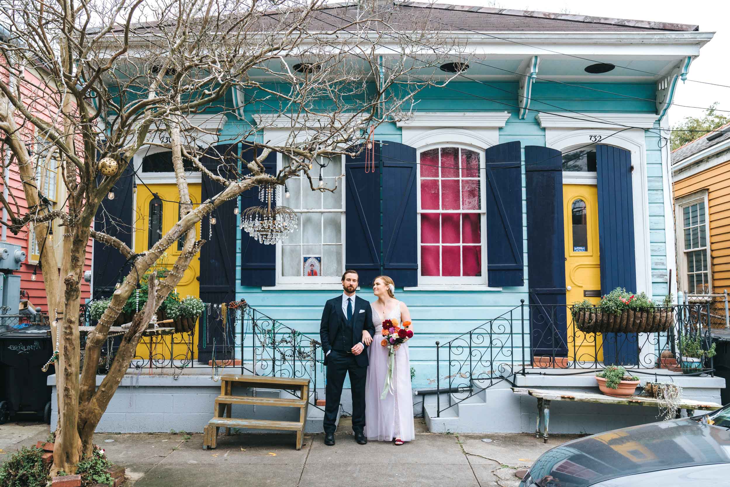 bride and groom standing next to each other in front of colorful blue house in the New Orleans Bywater