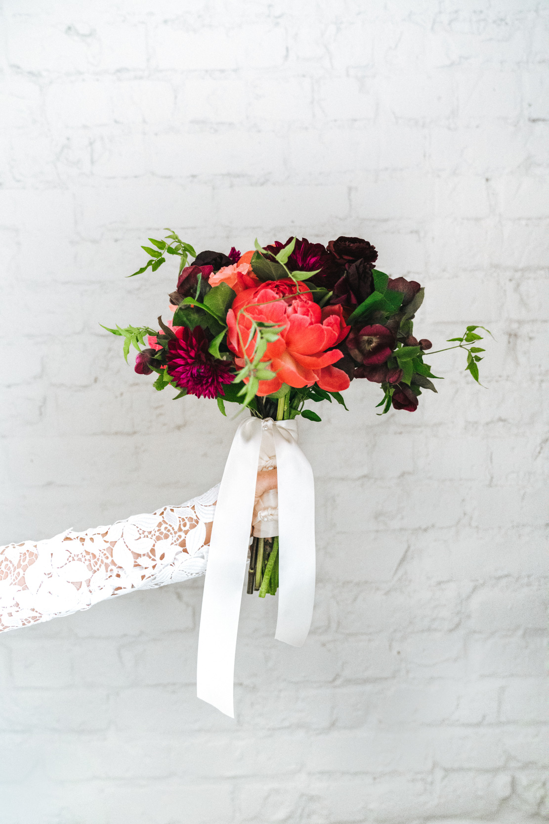 bride holding her bridal flowers and bouquet from Petals and Parties on wedding day against white brick wall at the Southern Hotel in Covington, Louisiana