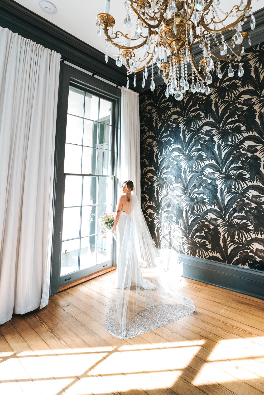 bride looking out of window while holding her Cicada Calling flowers with dress train at Margaret Place in New Orleans