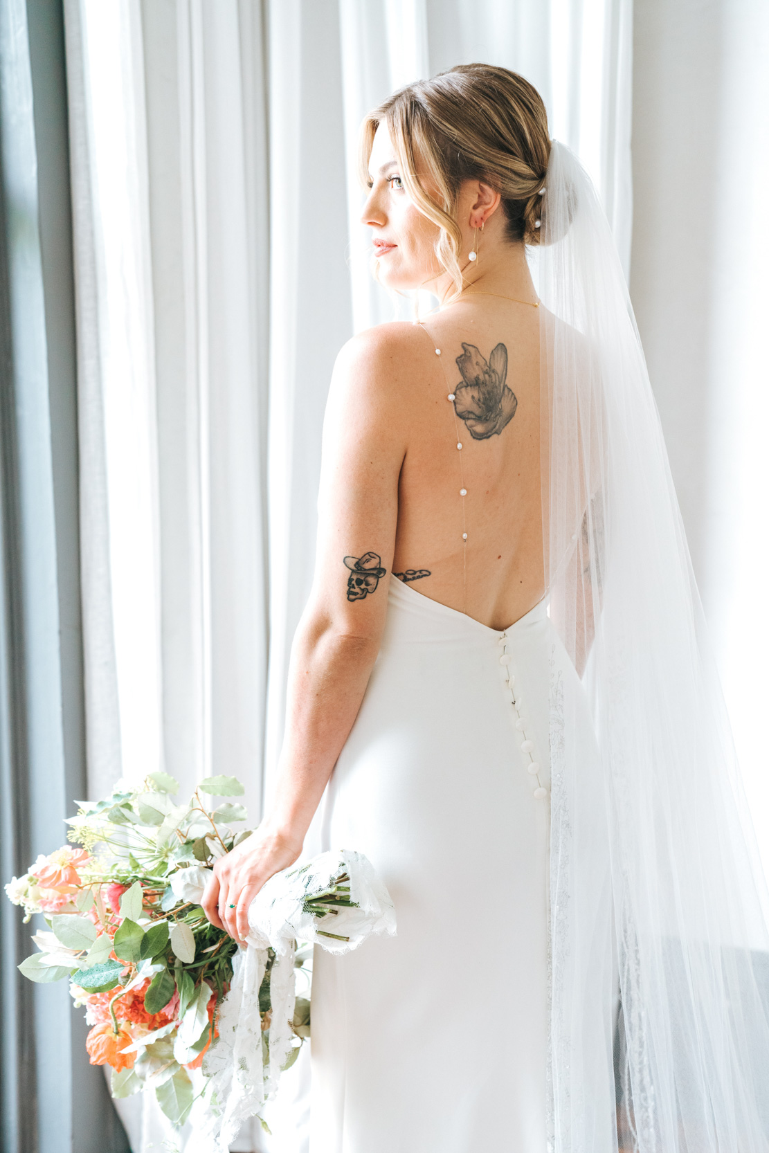 bride looking out window holding Cicada Calling flowers at Margaret Place in New Orleans