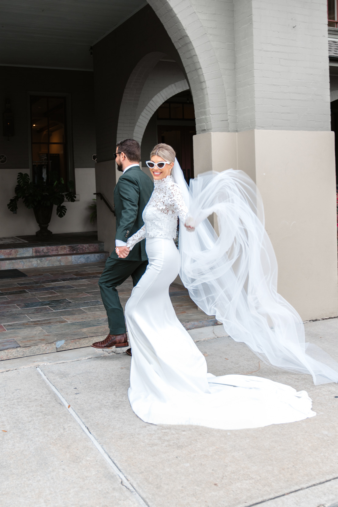 bride running along sidewalk and waving her wedding dress wearing 1965 Ashley Sievert glasses at the Southern Hotel in Covington, Louisiana