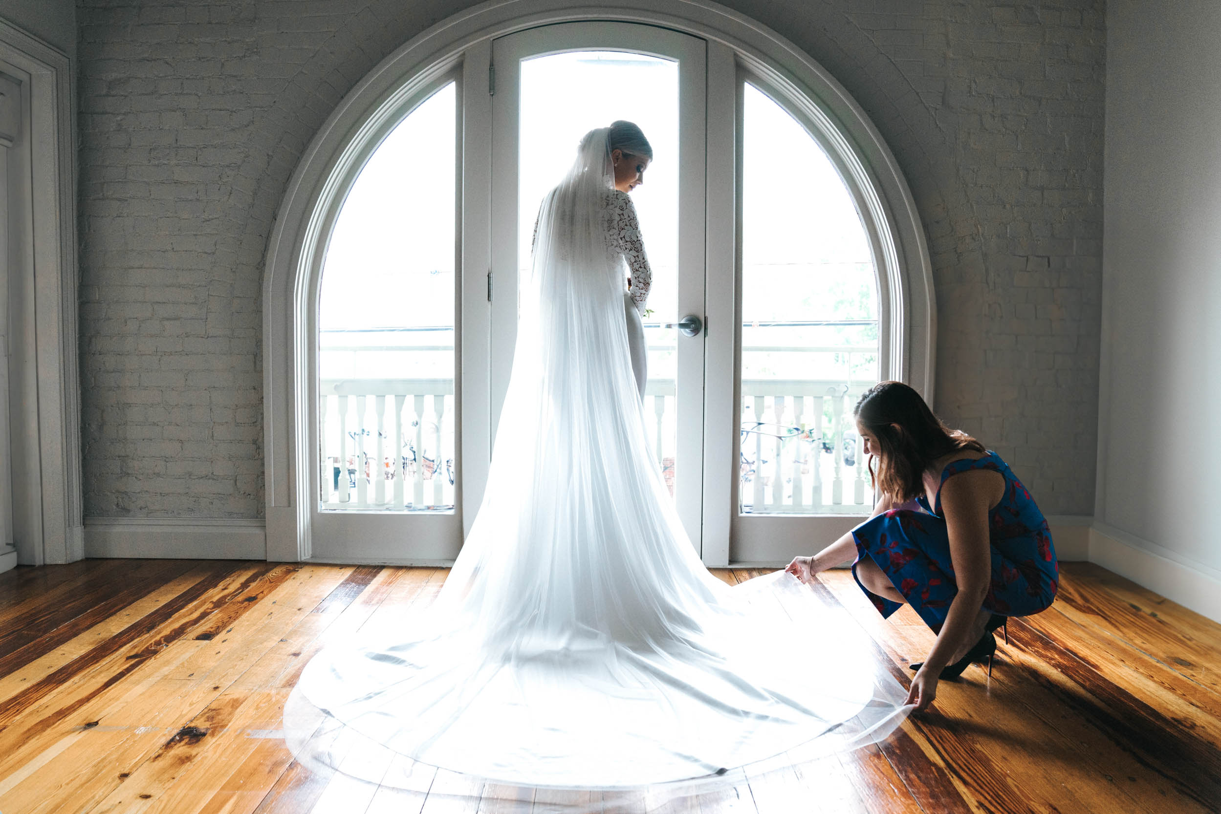 bridesmaid adjusting brides wedding dress in front of window in Thomas Sully bridal suite at the Southern Hotel in Covington, Louisiana