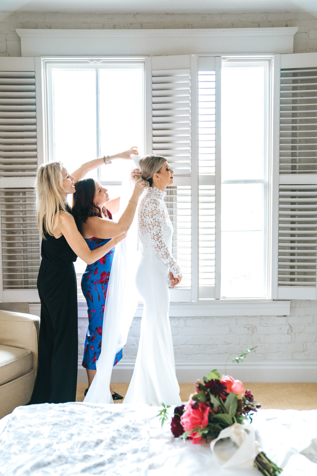 bridesmaids adjusting bride's veil in front of windows in the Thomas Sully bridal suite at the Southern Hotel in Covington, Louisiana