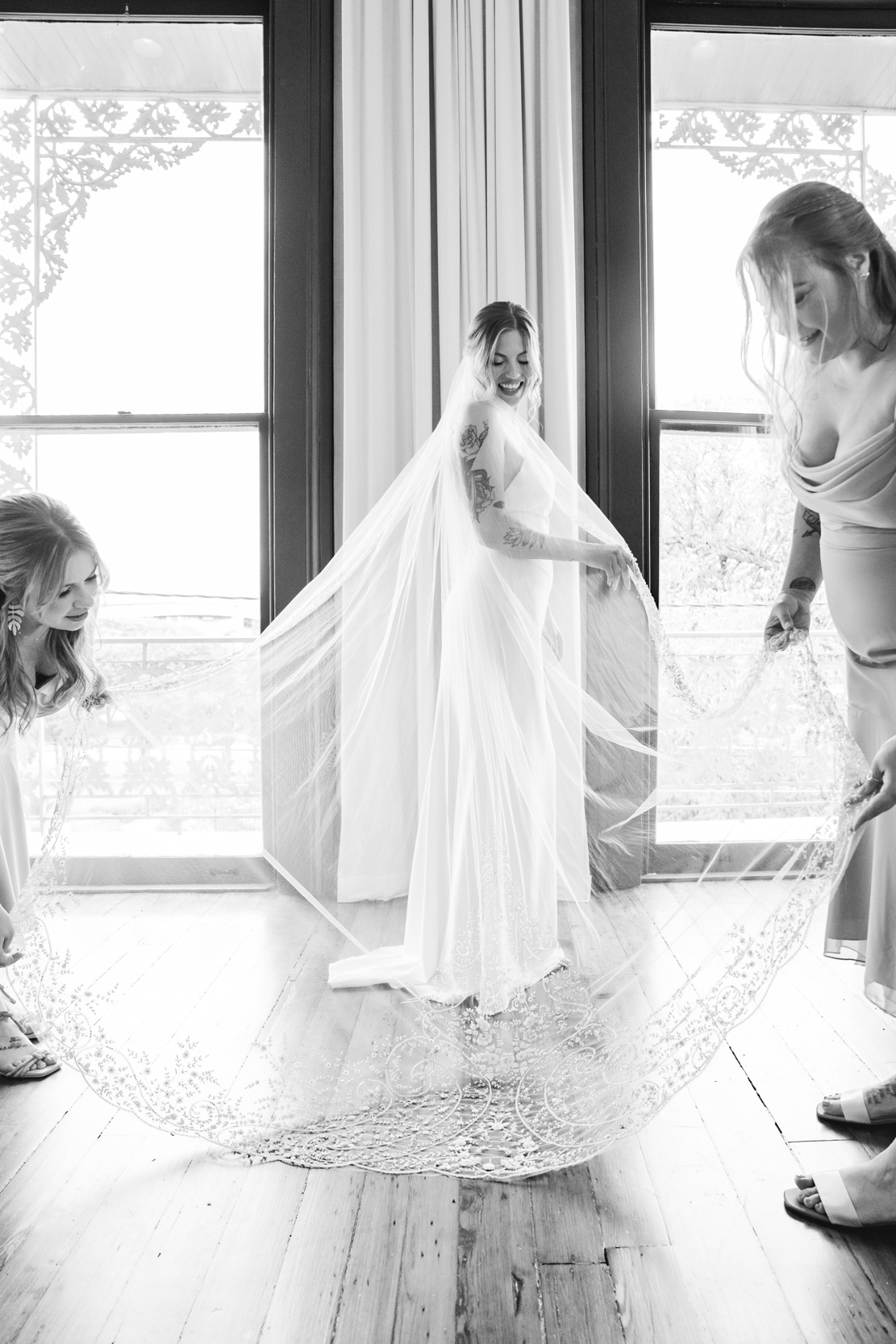 bridesmaids adjusting bride's wedding dress in front of windows in bridal suite at Margaret Place in New Orleans