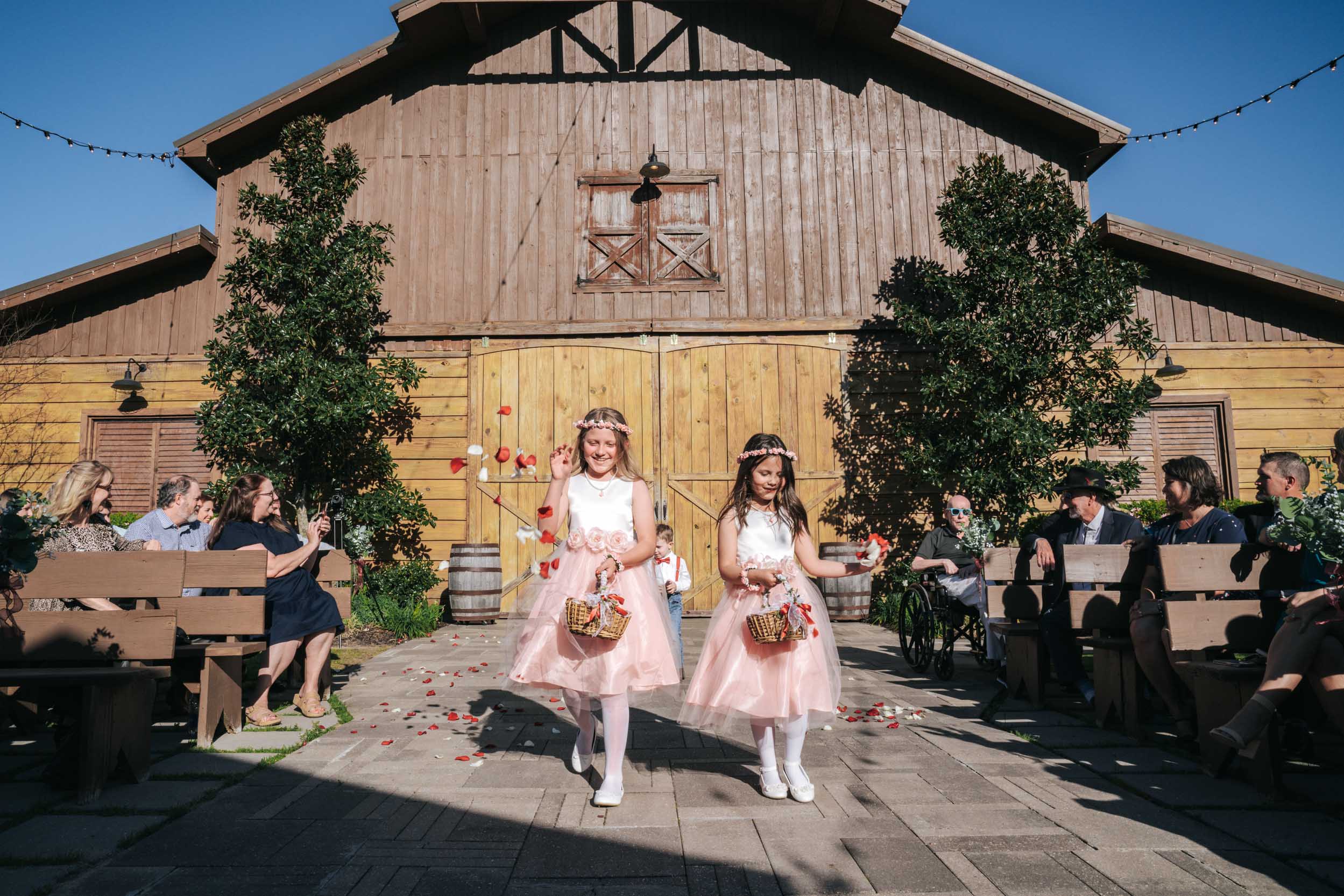 flower girls throwing flowers at a wedding in front of a barn at Berry Barn in Amite, Louisiana