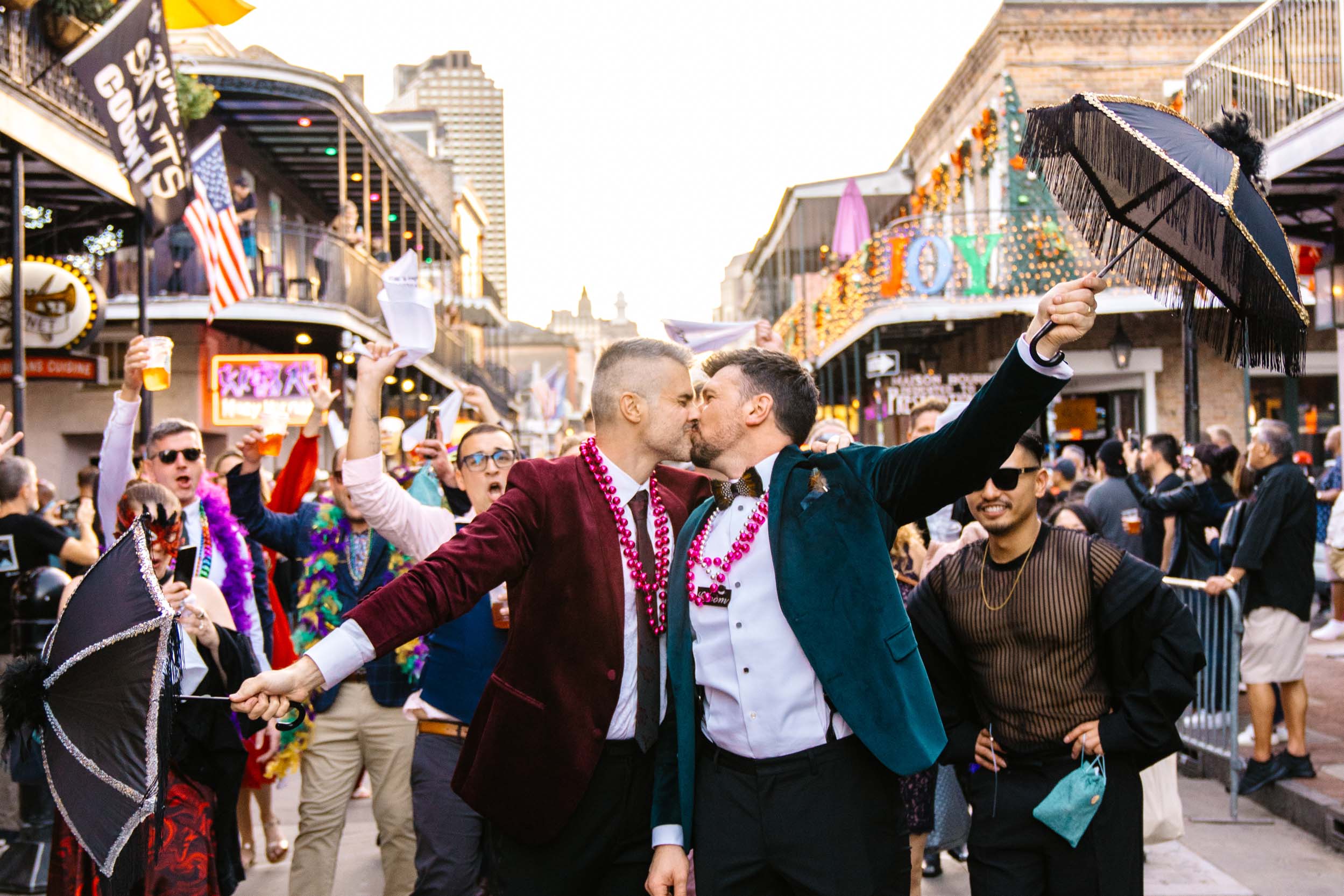 gay couple kissing on Bourbon Street in New Orleans during a 2nd Line band procession on their wedding day