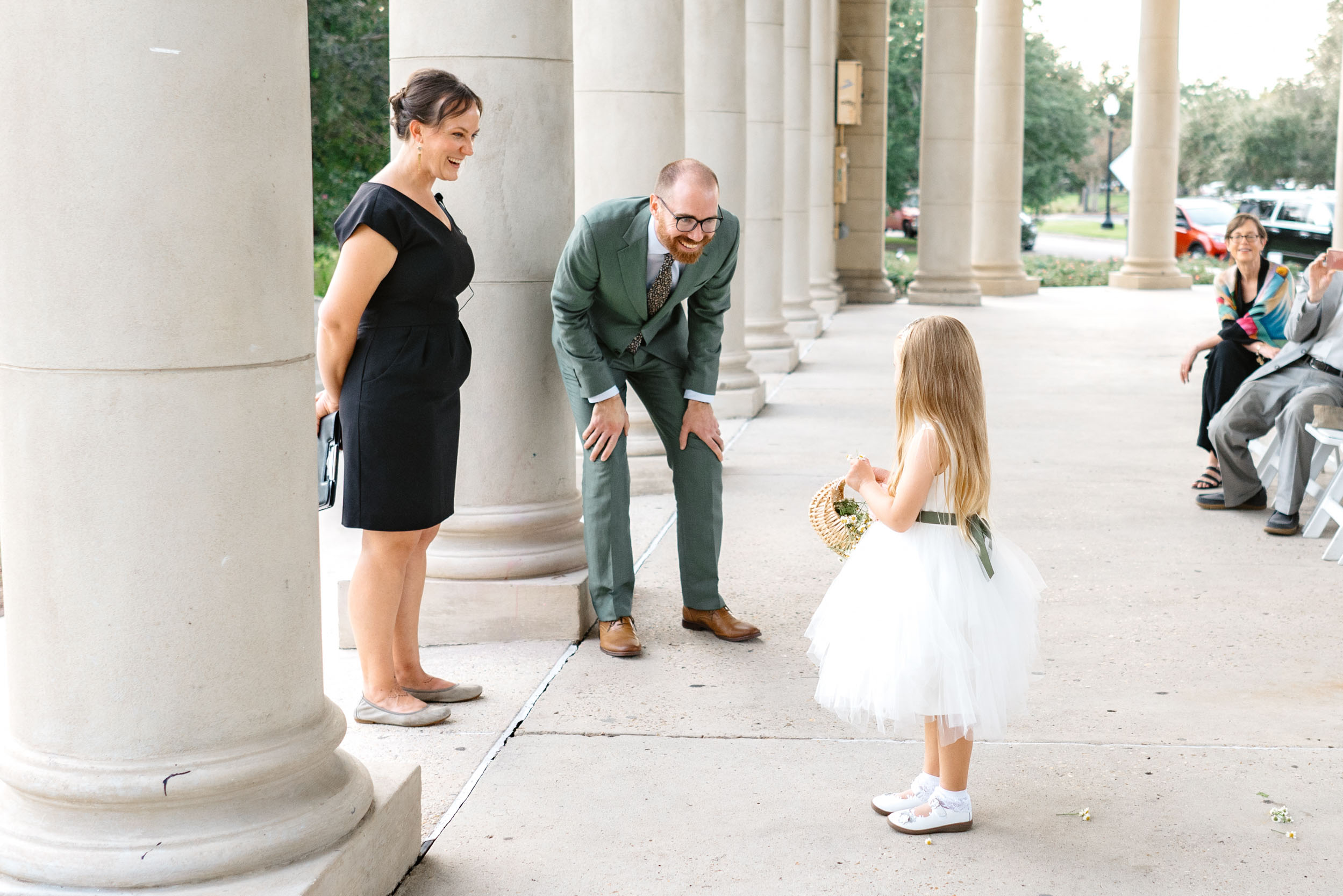 groom bending over smiling at flower girl during wedding ceremony under peristyle in City Park New Orleans