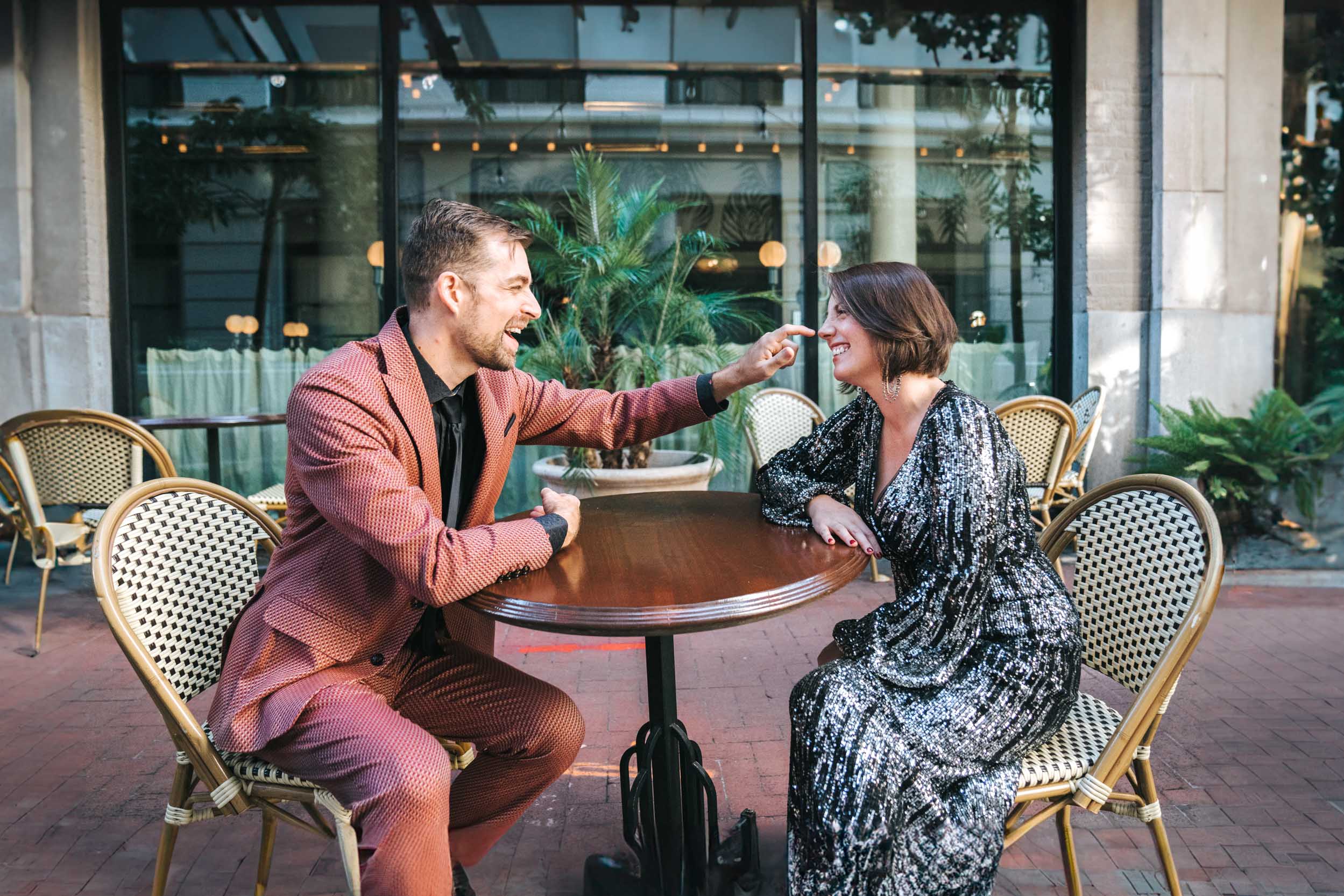 groom poking bride's nose while sitting at a table outside of the Ace Hotel in New Orleans