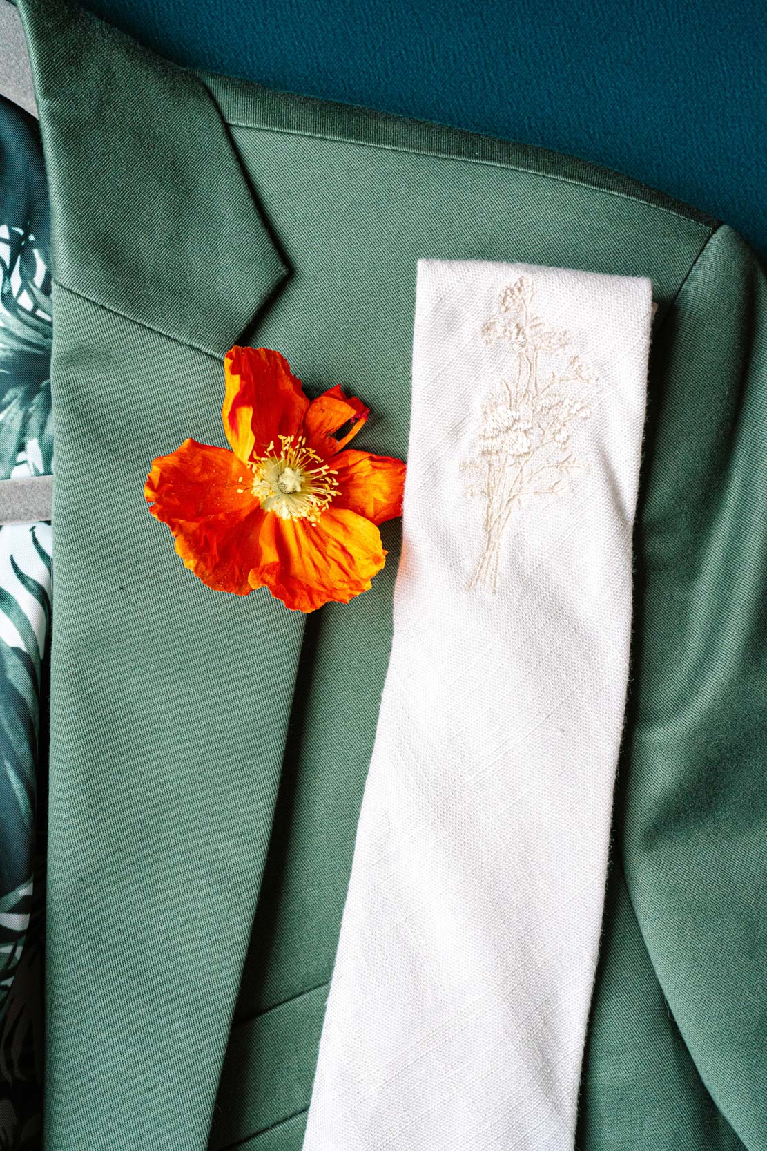 groom's green suit with ivory tie and red flower boutonniere at Margaret Place in New Orleans