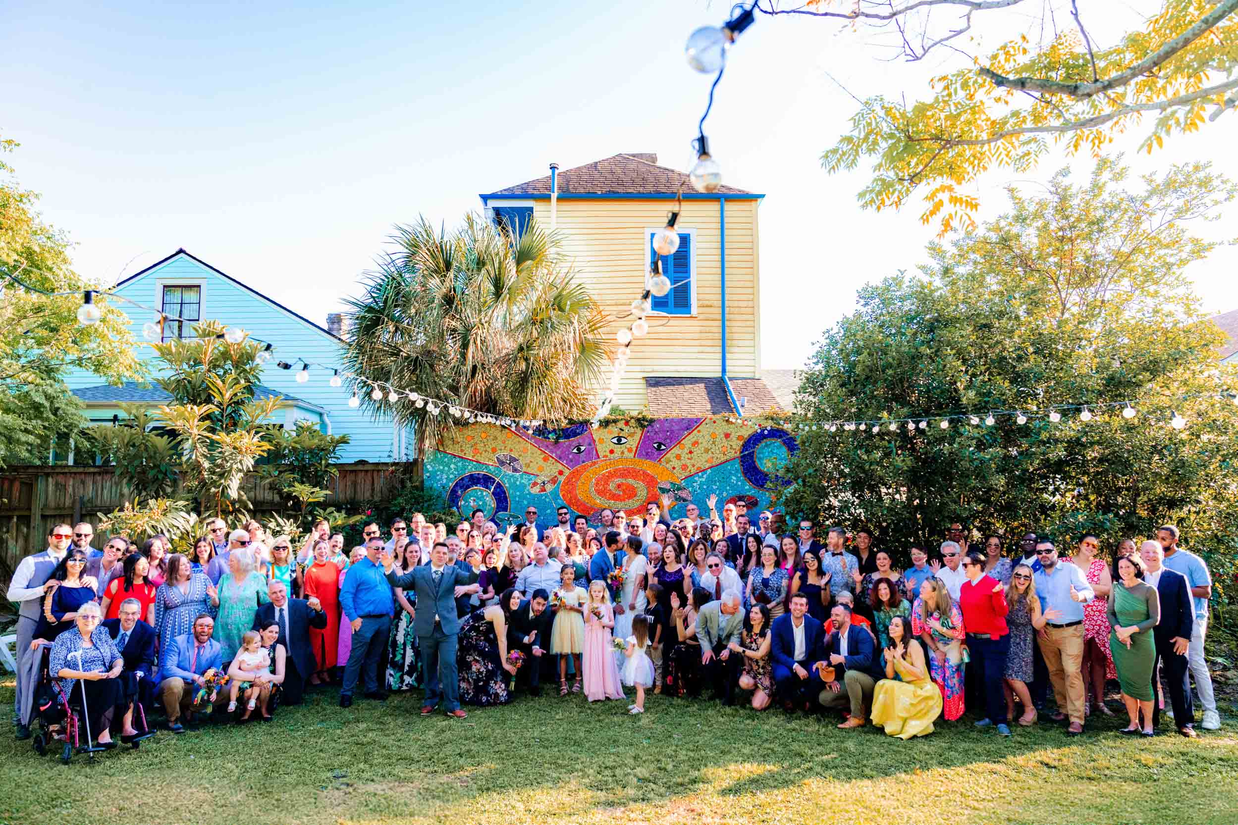 large group wedding photo on sunny day in front of colorful mural at Clouet Gardens in the Bywater of New Orleans