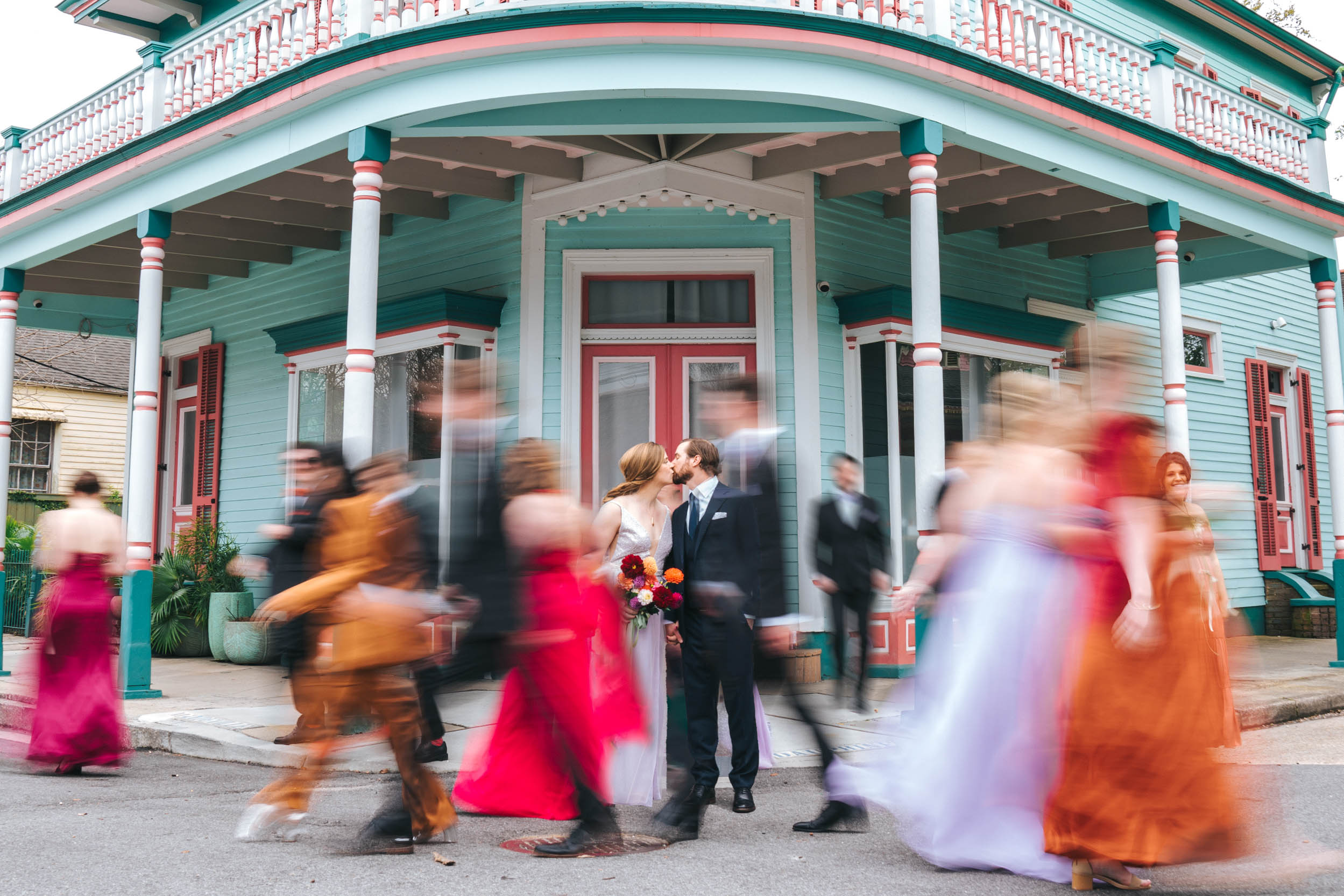 motion blur photograph of wedding party walking around bride and groom in the New Orleans Bywater in front of a colored house