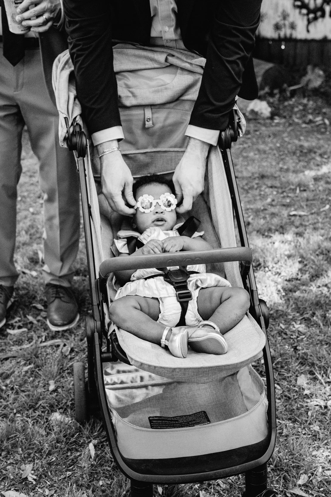 wedding guest adjusting baby's sunglasses in baby carriage during wedding ceremony at Clouet Gardens in the Bywater of New Orleans