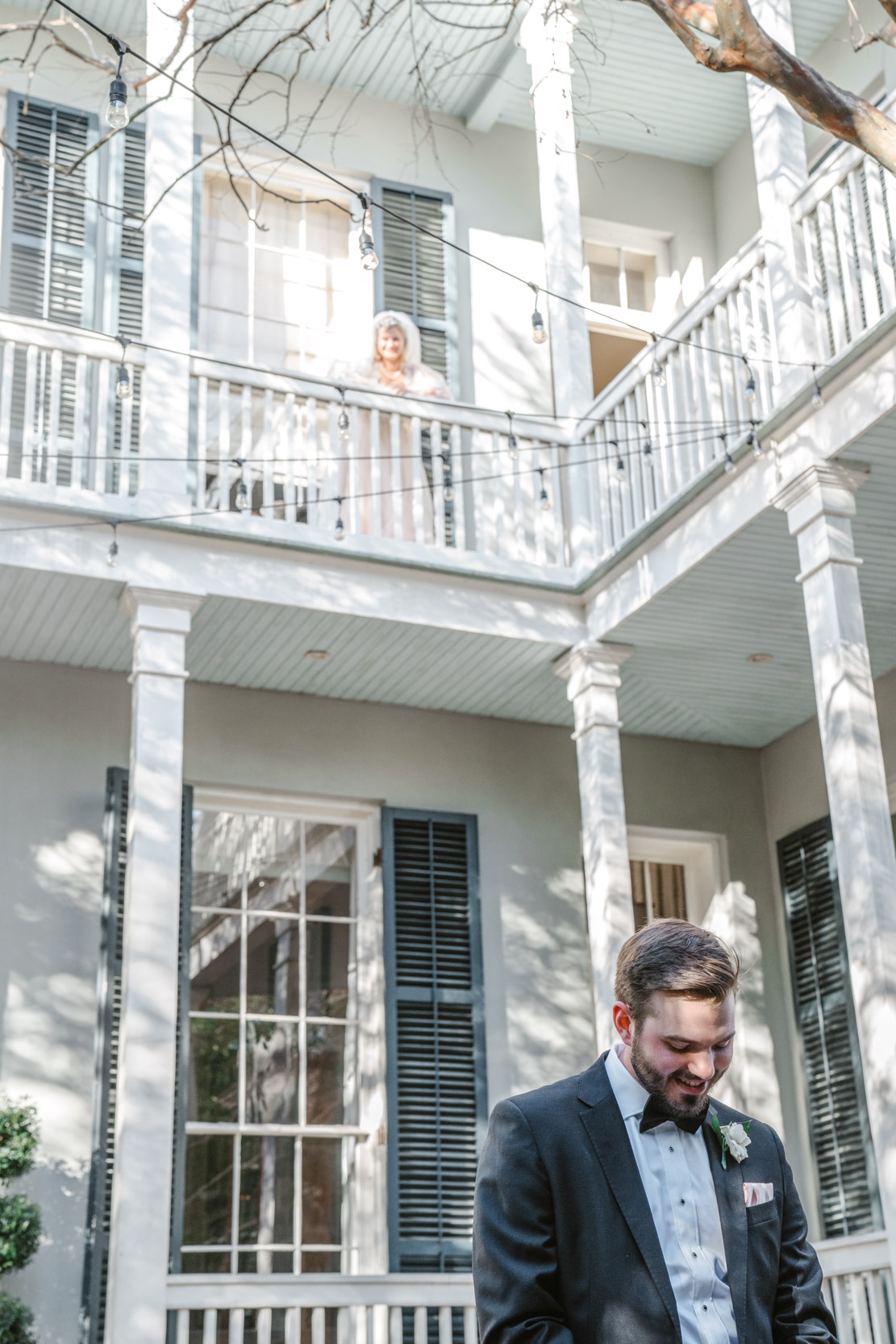 bride looking down at groom from balcony in courtyard during first look at the Terrell House in the New Orleans Lower Garden District