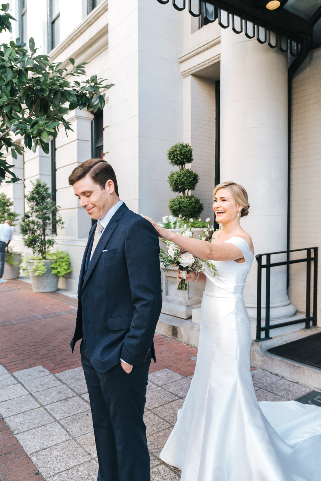 bride tapping groom's shoulder during first look on wedding day in front of the Maison De La Luz Hotel in New Orleans