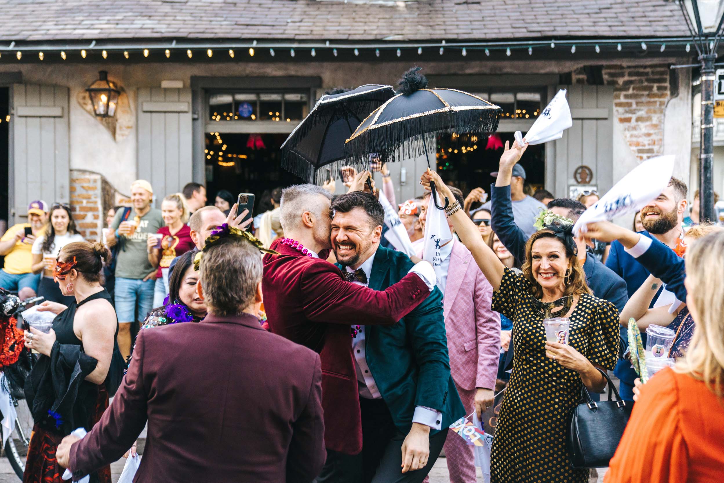 gay wedding couple celebrating with their parasols and wedding guests and 2nd line band in the French Quarter New Orleans