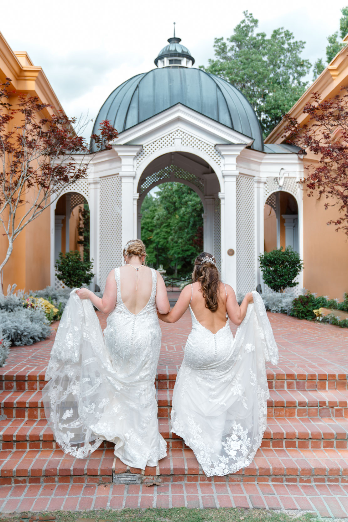 two brides holding their dresses and walking in the Botanical Gardens on gay wedding day at Pavilion of the Two Sisters in New Orleans