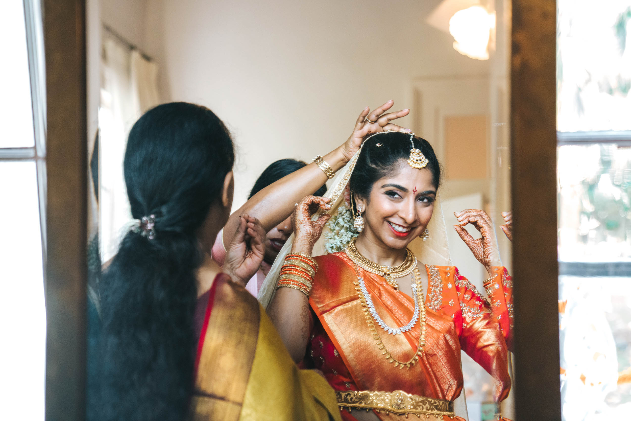 American Indian bride adjusting her veil while her family put her lehenga or a saree wedding dress on at Derbès Mansion in New Orleans