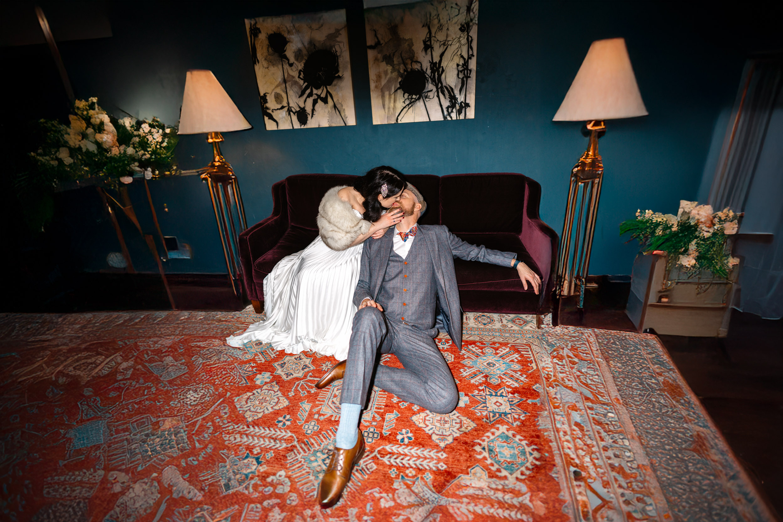 Flash photo of bride kissing groom sitting on ground in front of couch at The Eliza Jane Hotel in New Orleans