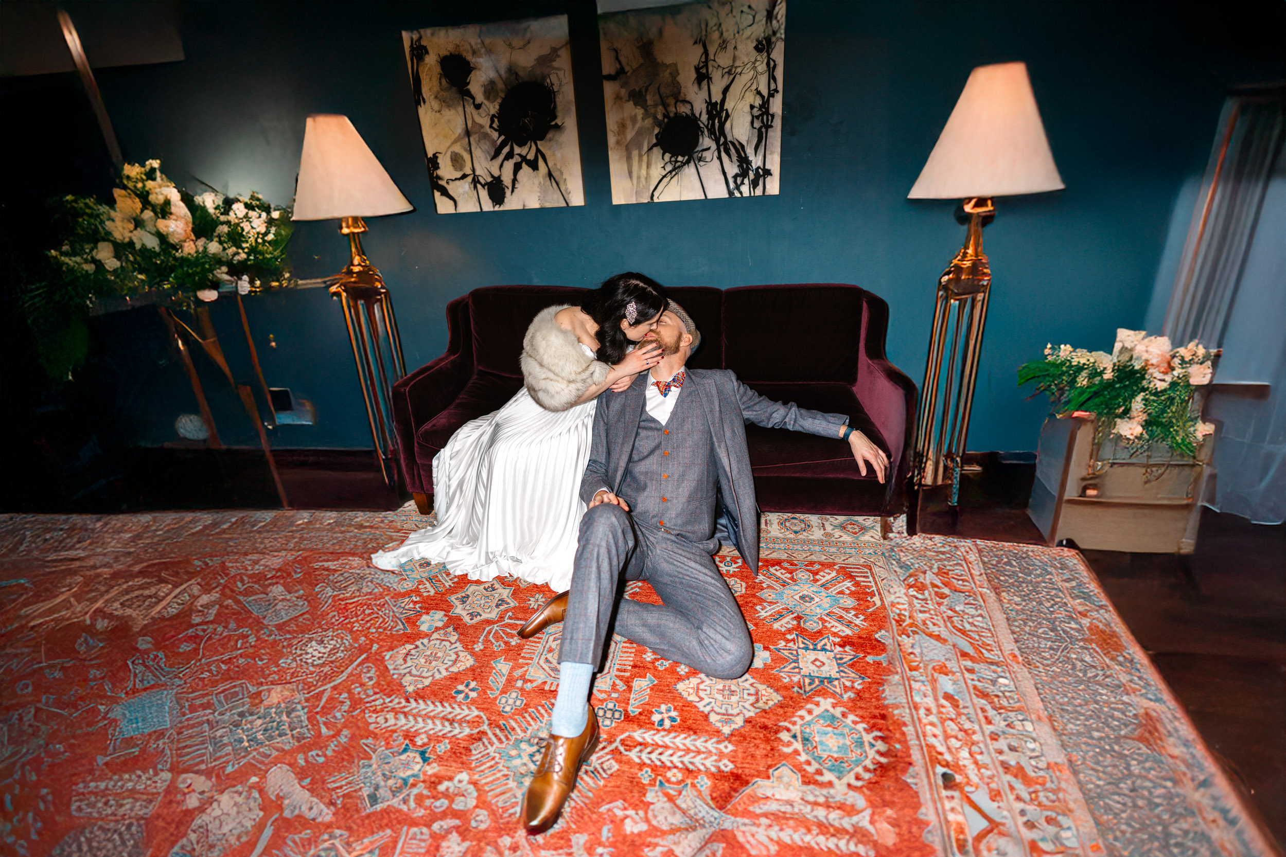 Flash photo of bride kissing groom sitting on ground in front of couch at The Eliza Jane Hotel in New Orleans-Edit