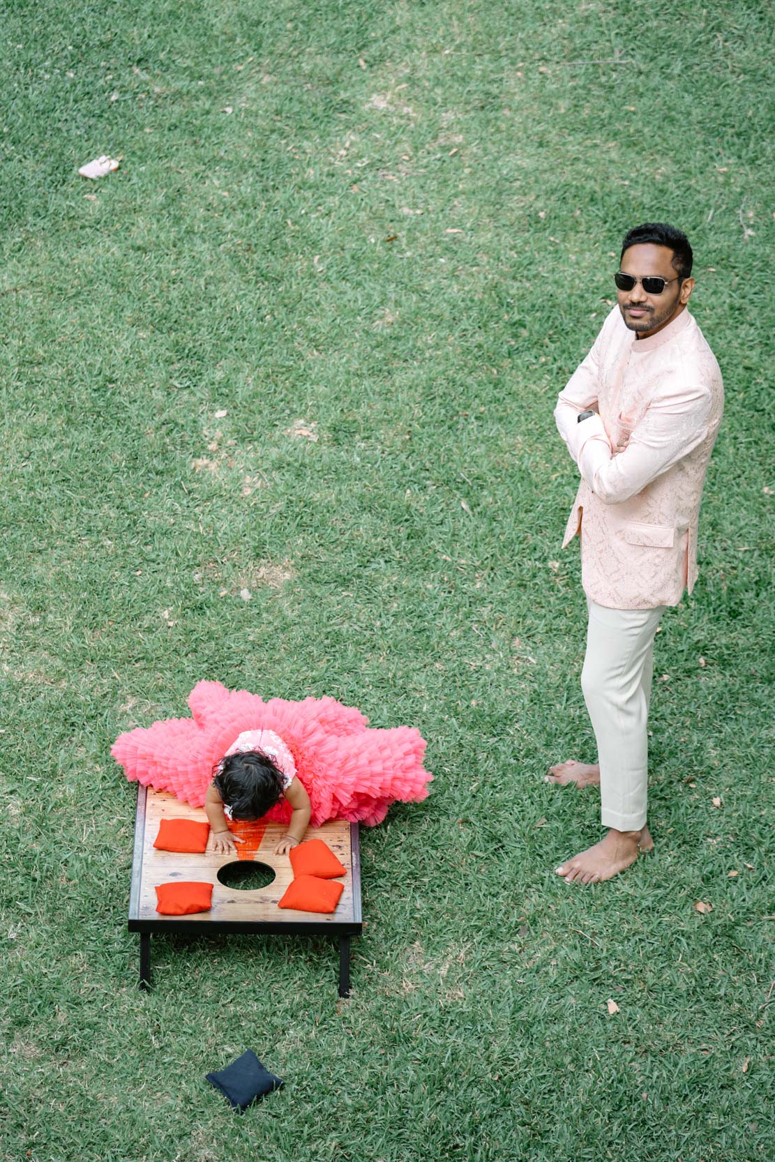 Islamic or Hindu wedding guest watching his daughter crawl on a cornhole game device before nikah ceremony at Derbès Mansion in New Orleans