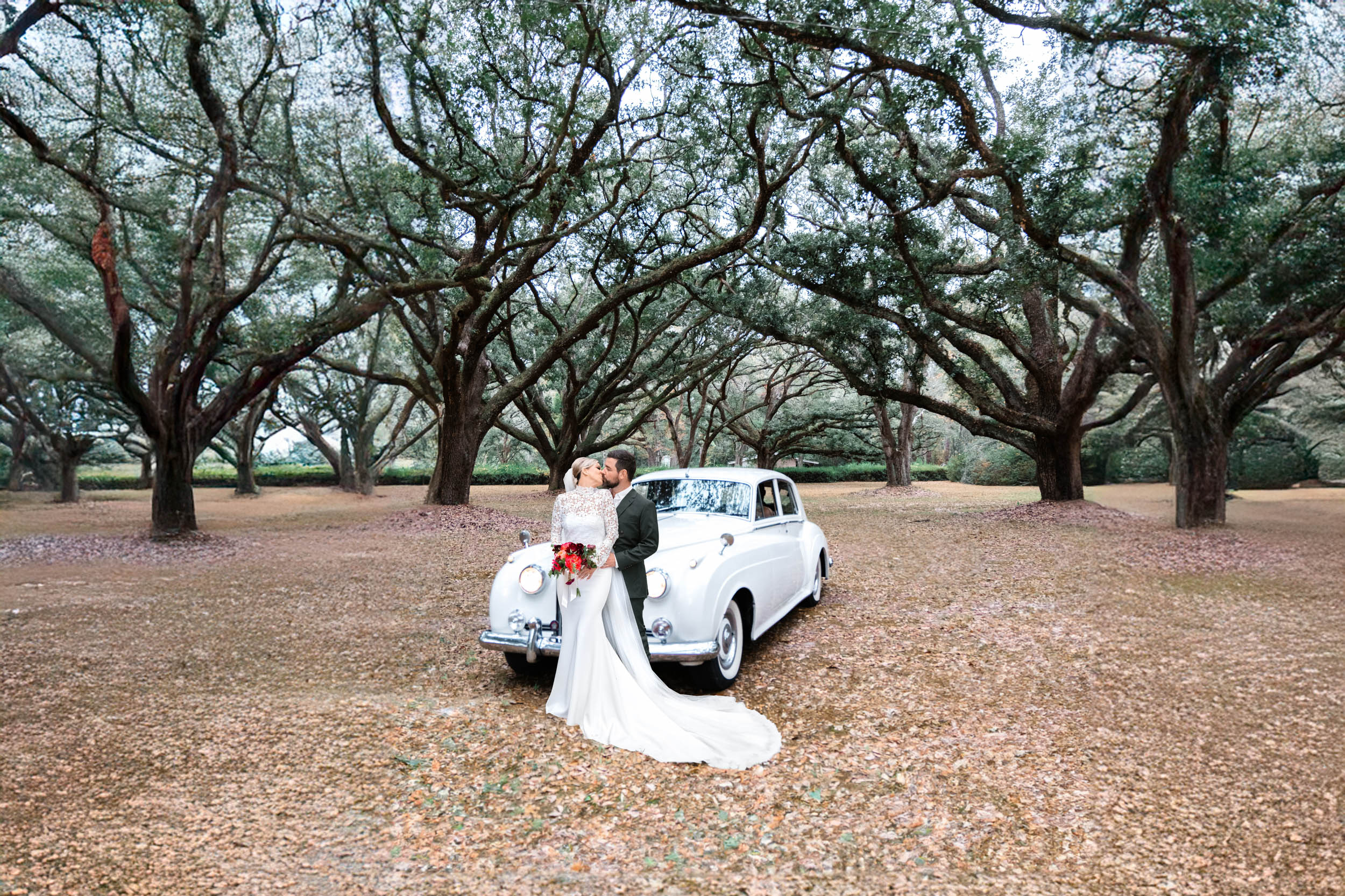 bride and groom kissing in front of Rolls-Royce and large oak trees at The Greenwood Covington, Louisiana