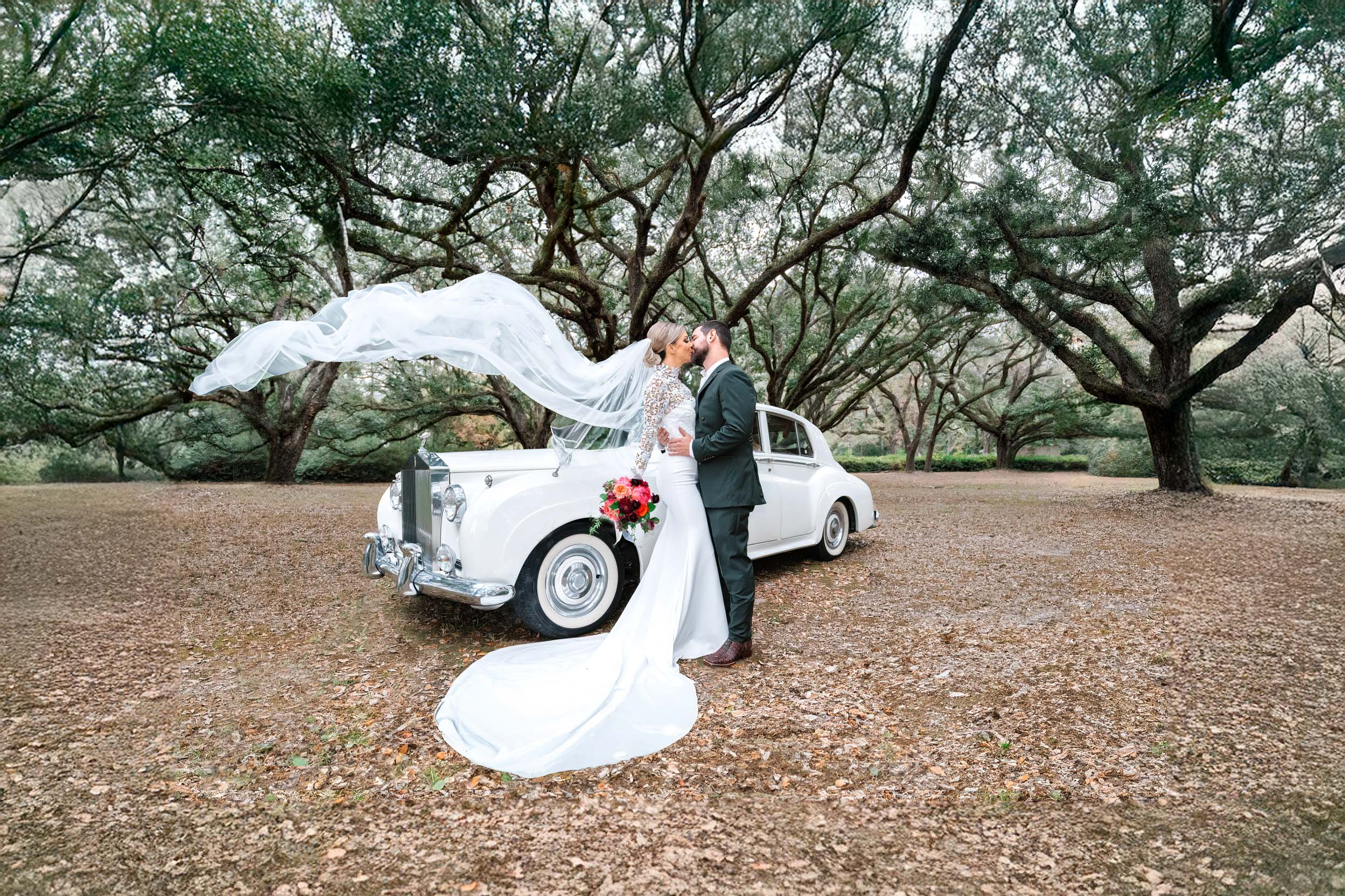 bride and groom kissing with veil flying in the air in front of Rolls-Royse and large oak trees at The Greenwood Covington, Louisiana