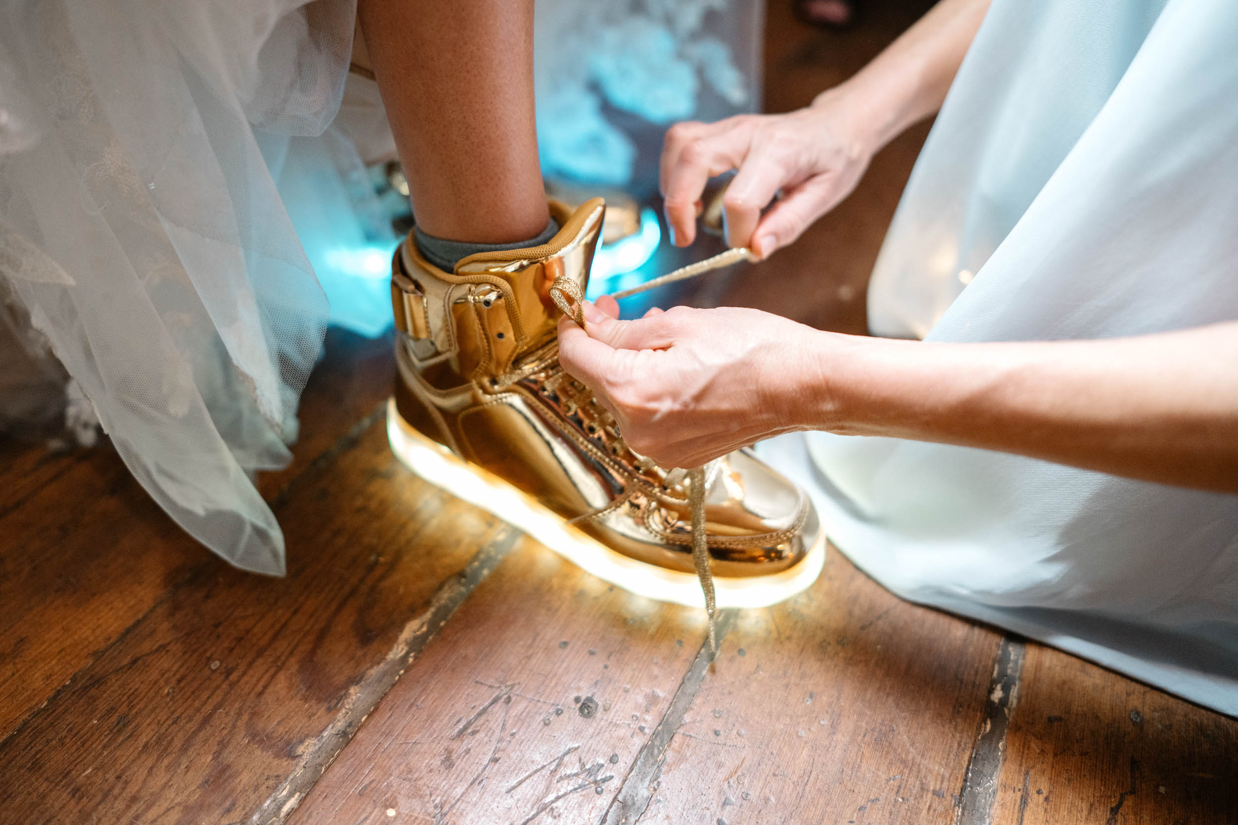 gold light up tennis shoes being tied during masquerade wedding reception at Hotel Peter and Paul in New Orleans Bywater