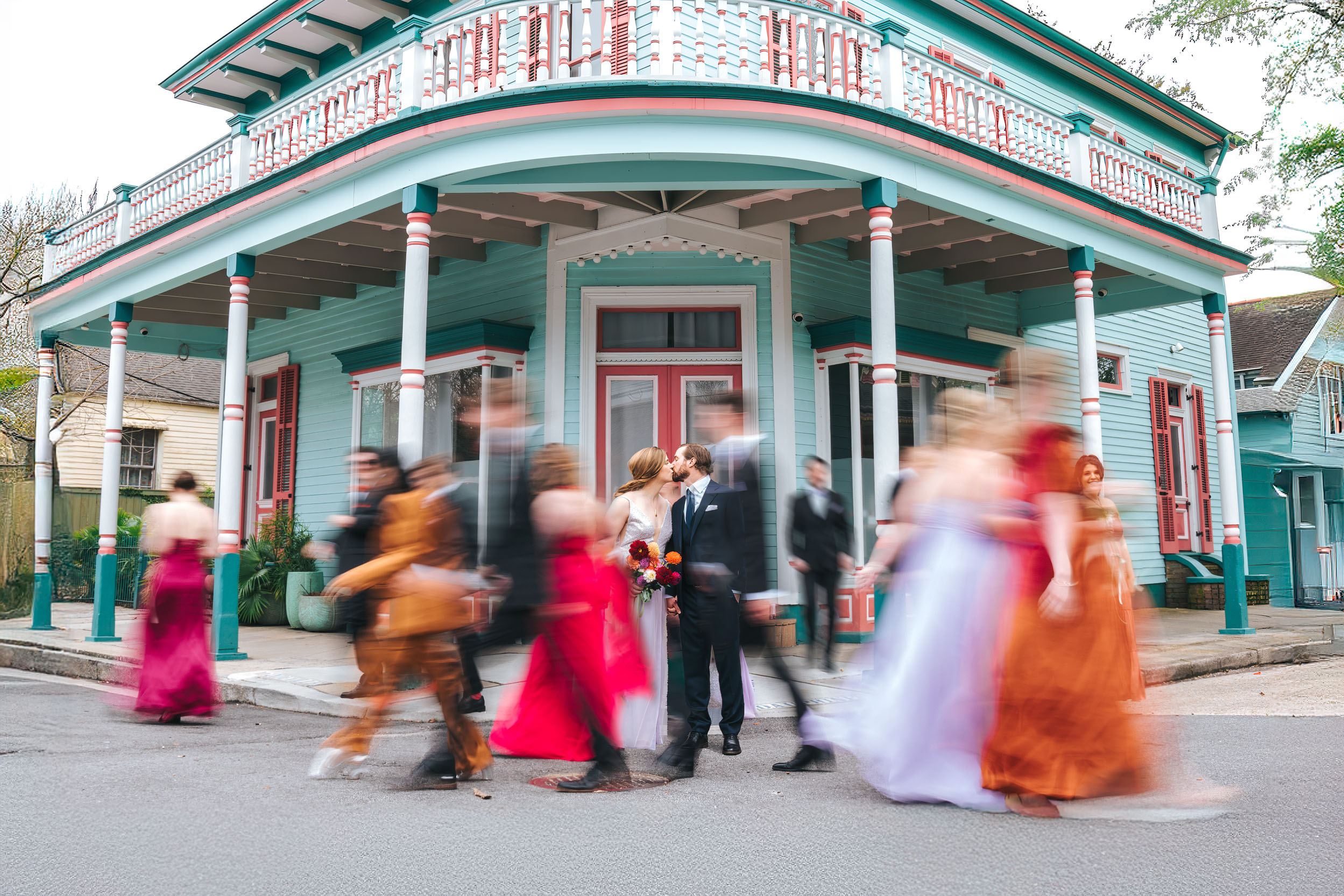 motion blur photograph of wedding party walking around bride and groom in the New Orleans Bywater in front of a colored house